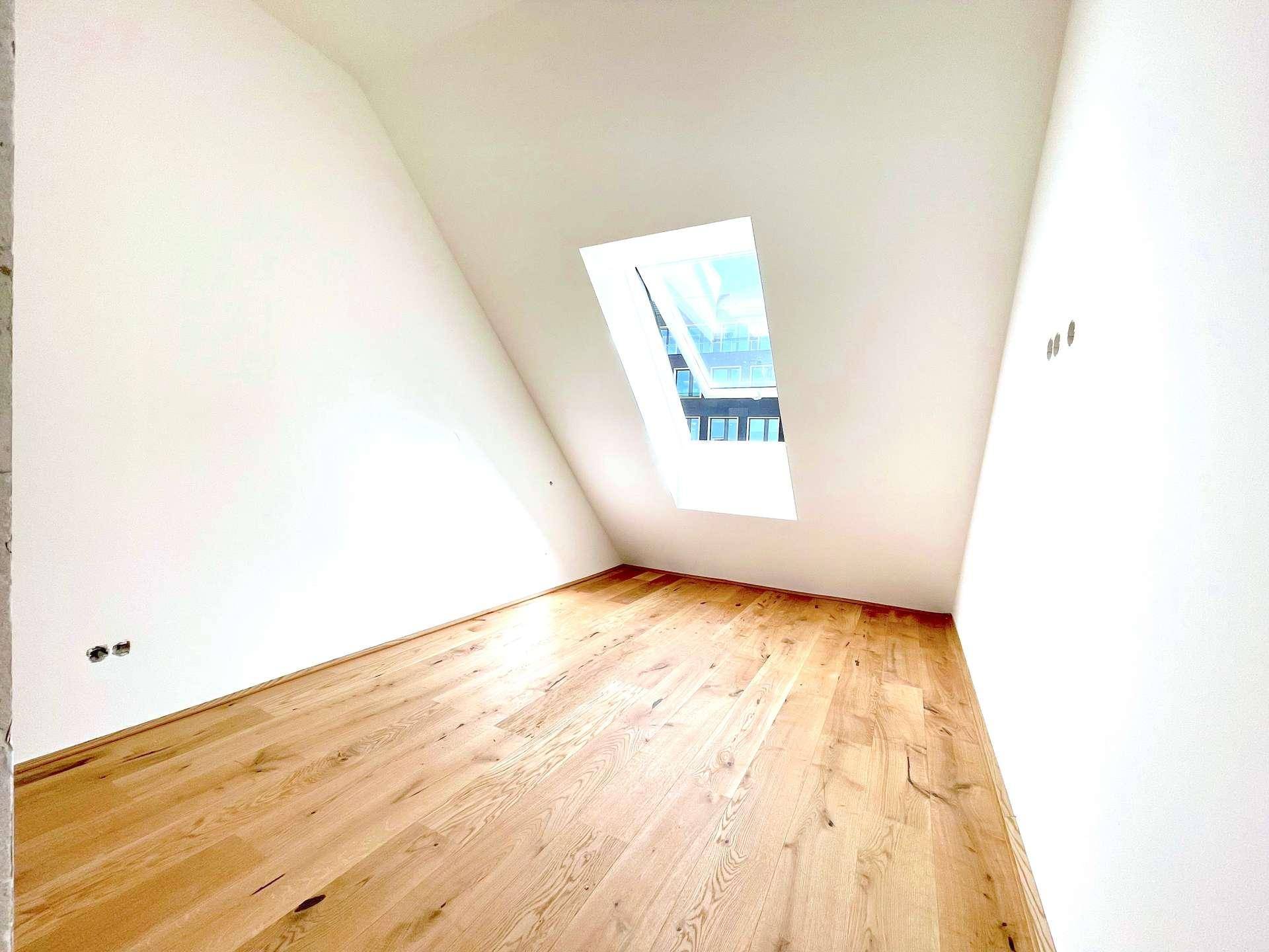 Helles Dachgeschosszimmer mit Holzboden und einem einzelnen schrägen Dachfenster, ideal für Ruhe.