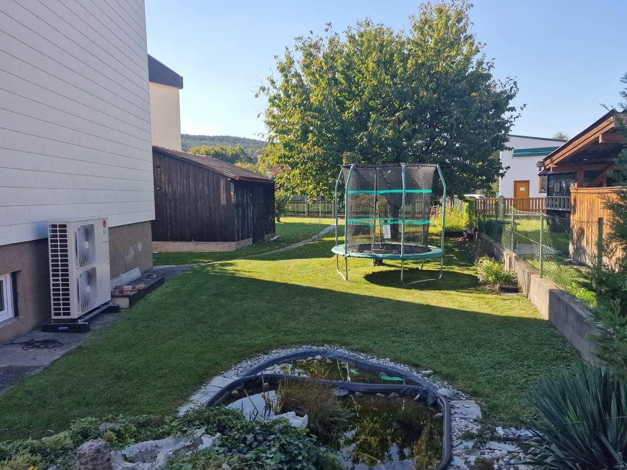 Großer Garten mit Rasenfläche, einem Teich und einem Trampolin.