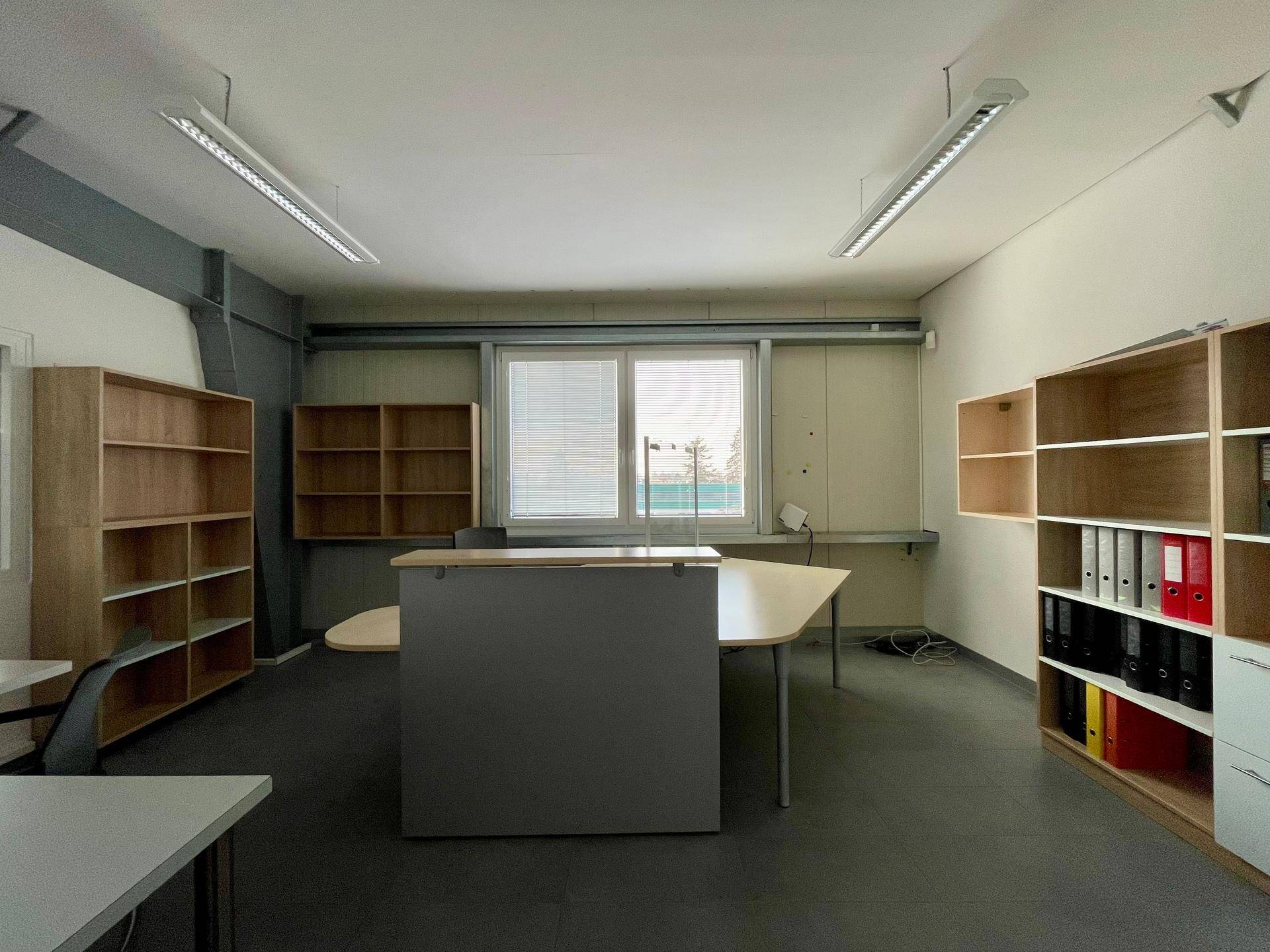 Funktionales Büro mit Holzregalen, grauem Schreibtisch und einem Fenster mit Jalousien, ideal für konzentriertes Arbeiten.