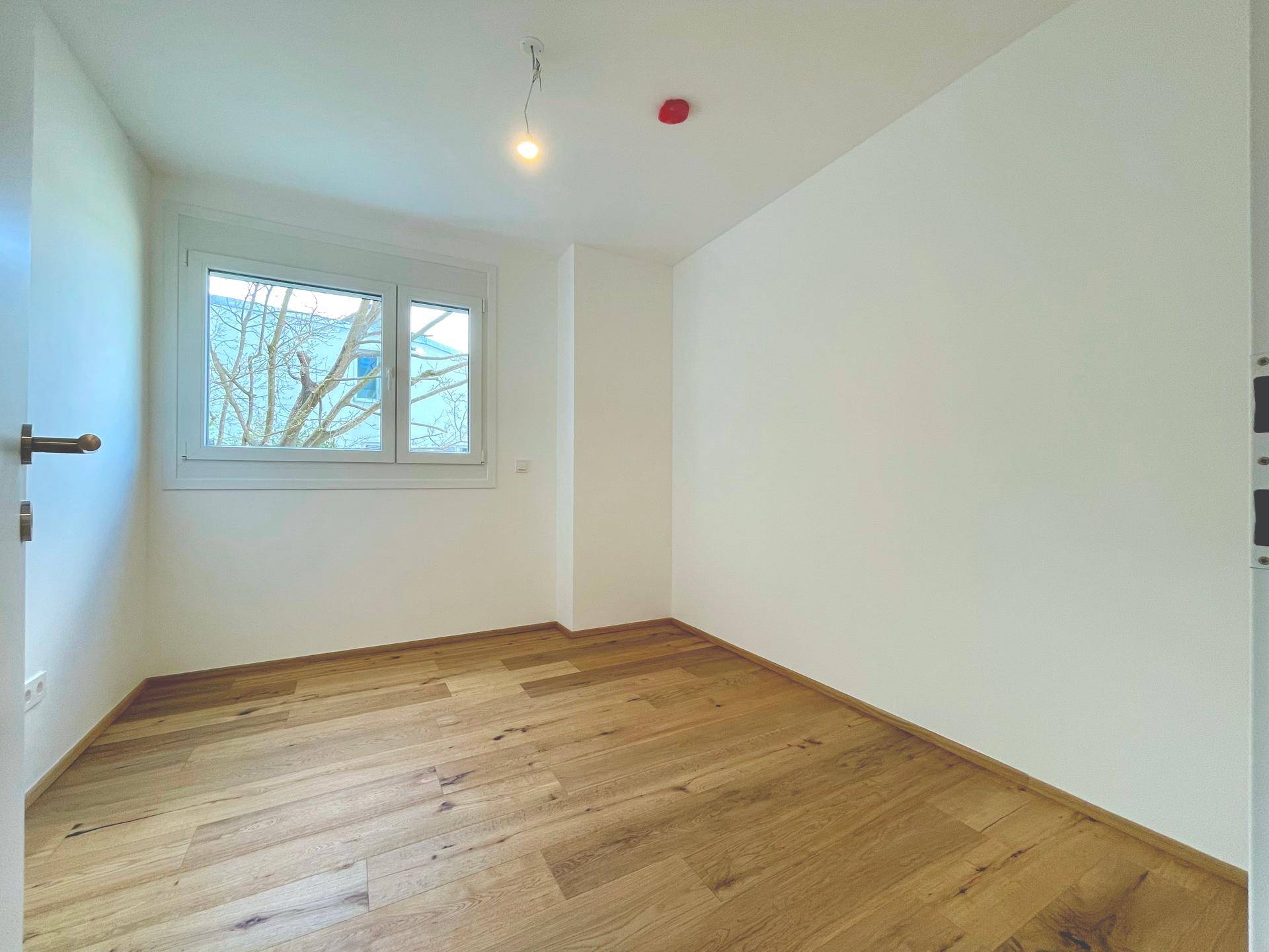 Helles Schlafzimmer mit Holzboden und Fenster, bietet eine ruhige und angenehme Atmosphäre.
