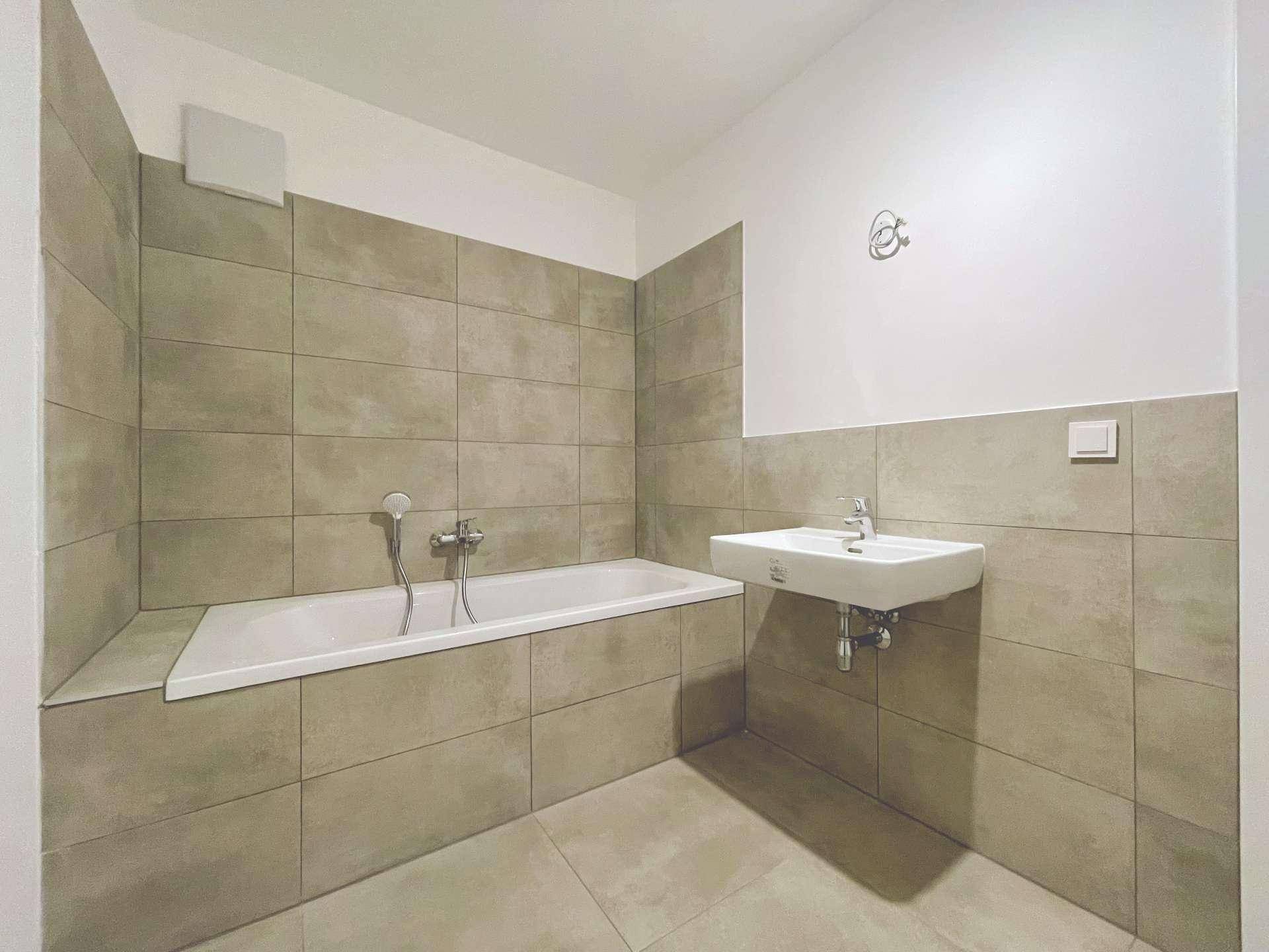Sauberes Badezimmer mit Badewanne und Waschbecken, ausgestattet mit modernen Armaturen und Fliesen.