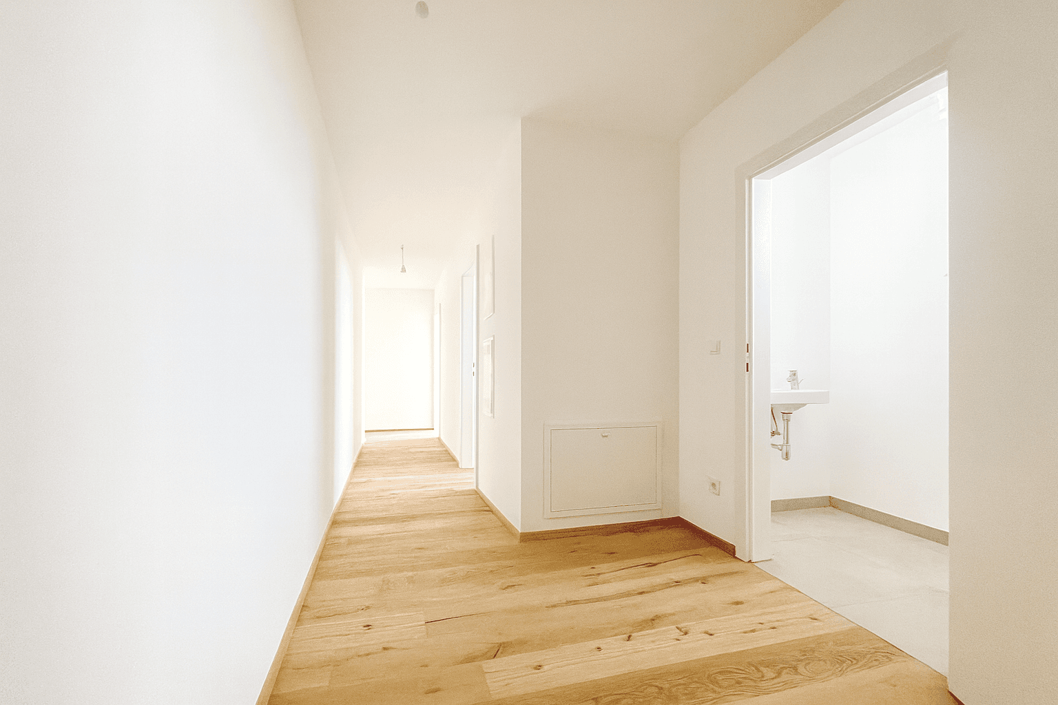 Heller, leerer Wohnraum mit Holzboden und großen Fenstern, die viel Tageslicht hereinlassen.