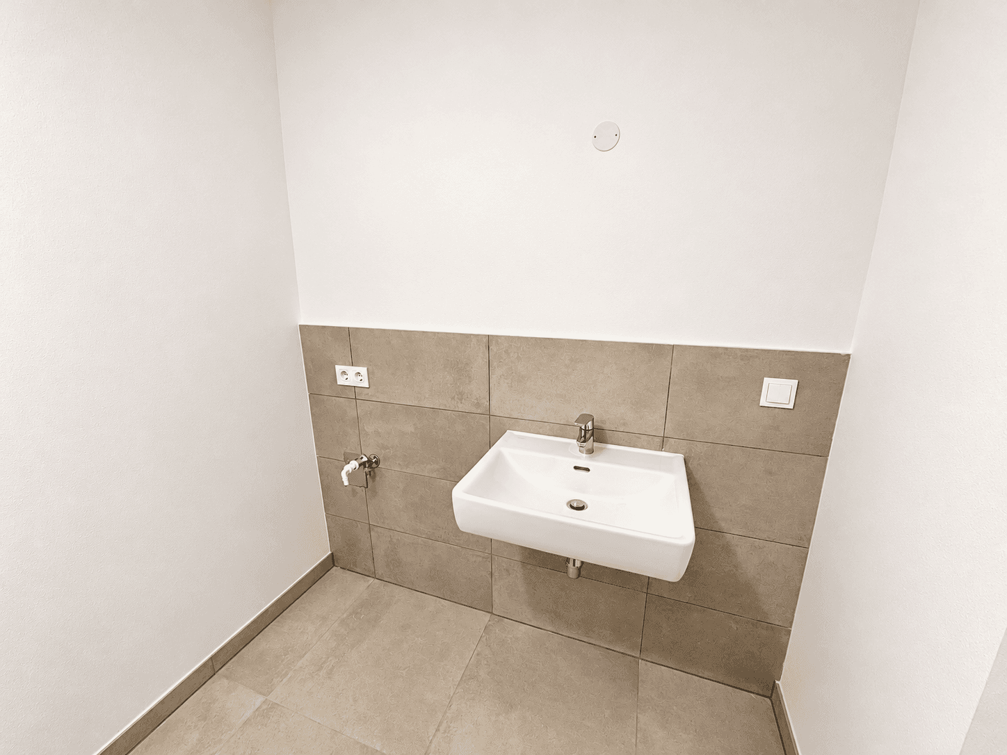 Kleines Gäste-WC mit Waschbecken und teilweiser Wandfliesenverkleidung in neutralen Farbtönen.