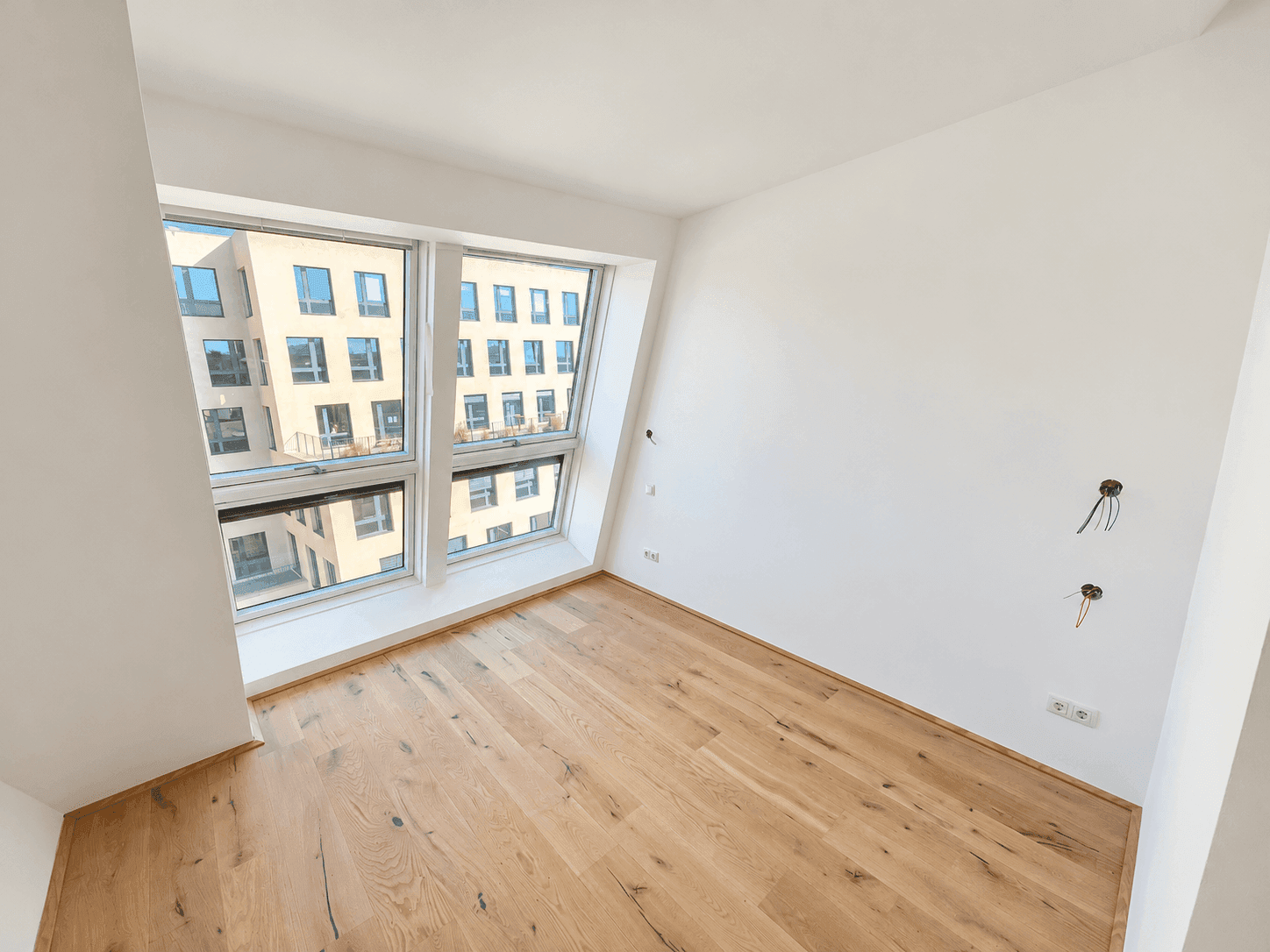Helles Zimmer mit Holzboden und großen Fenstern, die viel Tageslicht hereinlassen.