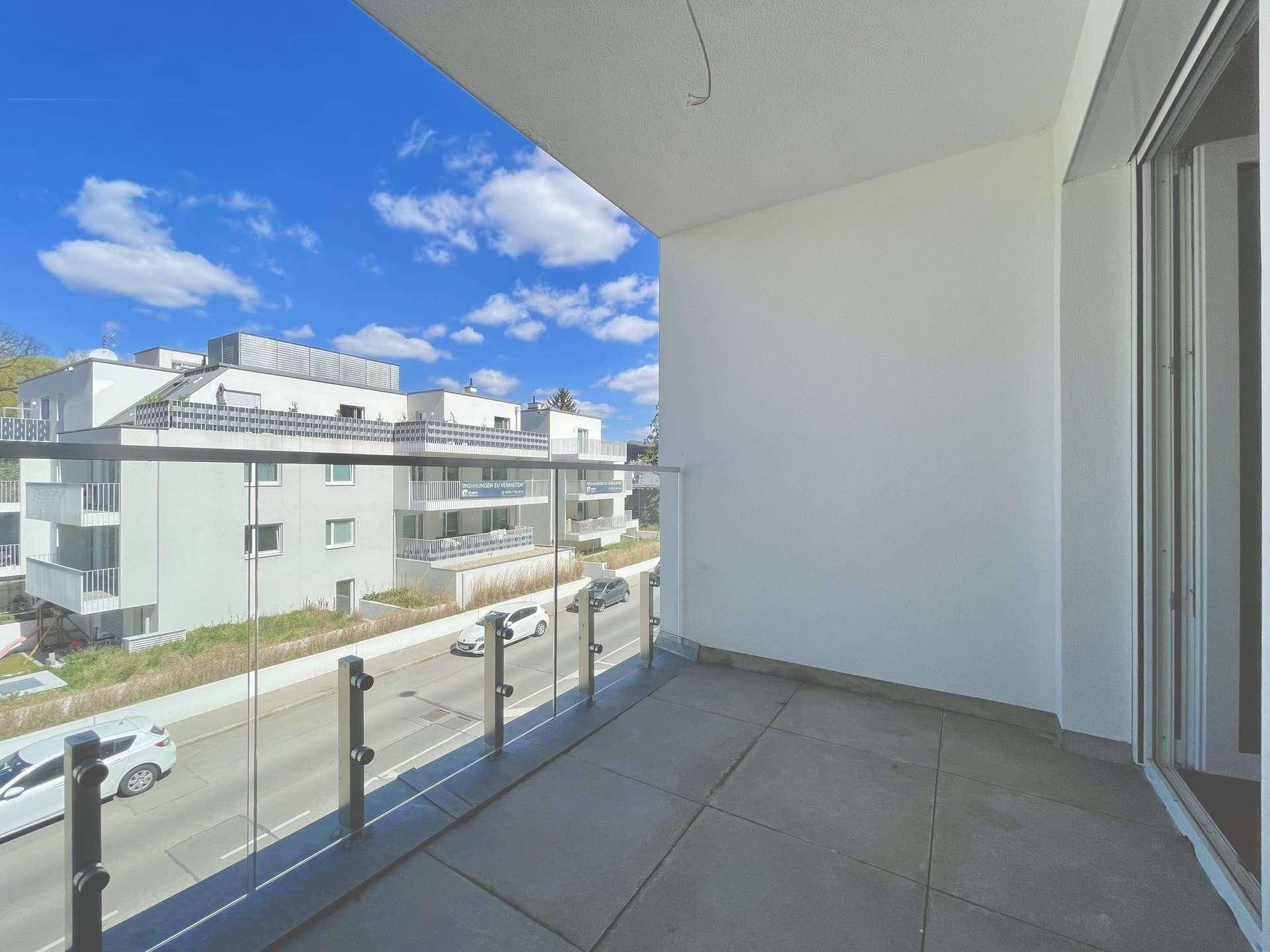 Moderner Balkon mit Glasgeländer und Blick auf die Straße und umliegende Gebäude.