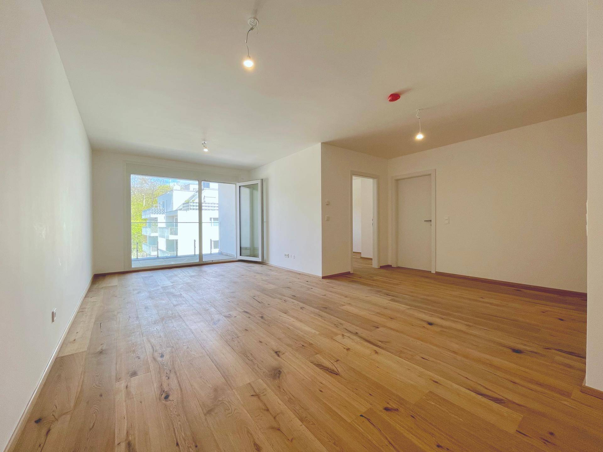 Helles Wohnzimmer mit Holzboden und Zugang zu einem Balkon, bietet viel Tageslicht und frische Luft.