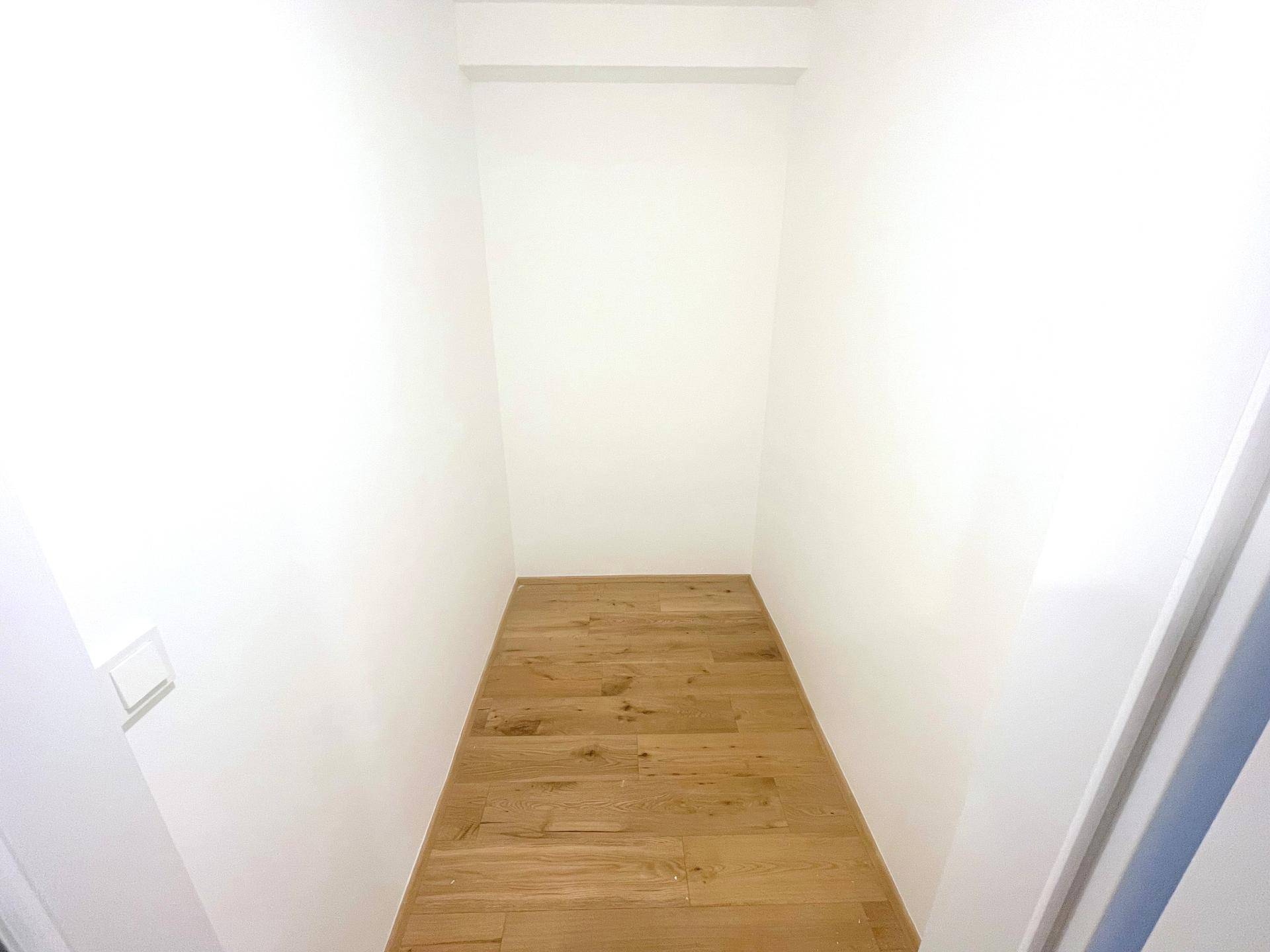 Schmaler Abstellraum mit Holzboden und weißen Wänden, ideal für zusätzlichen Stauraum.