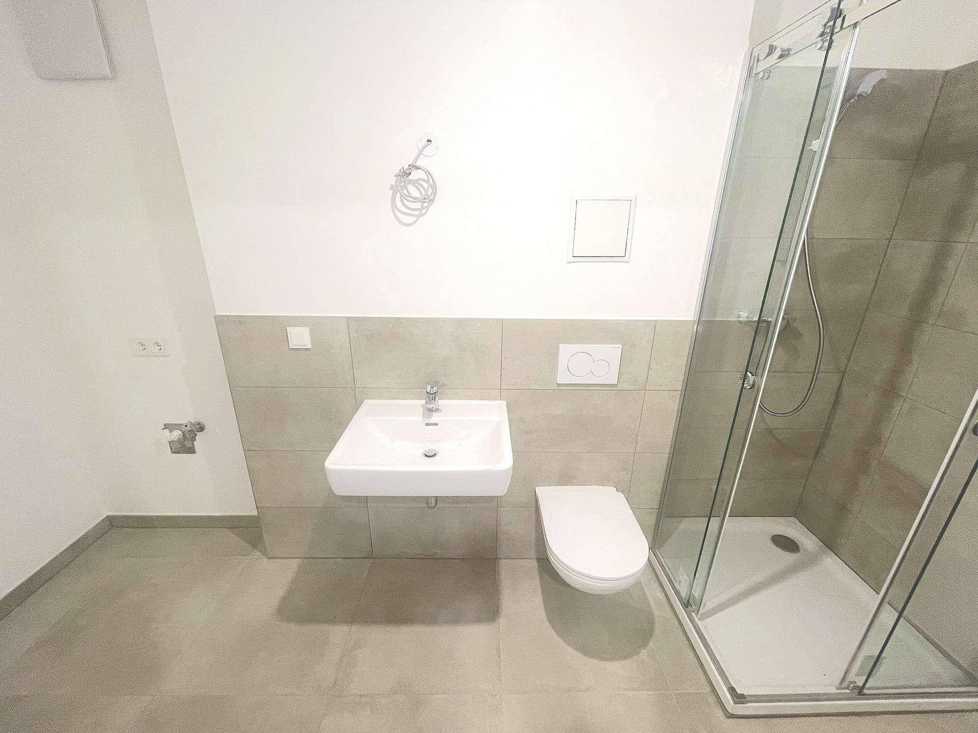 Modernes Badezimmer mit Duschkabine, wandhängendem WC und Waschbecken, ausgestattet mit grauen Fliesen.
