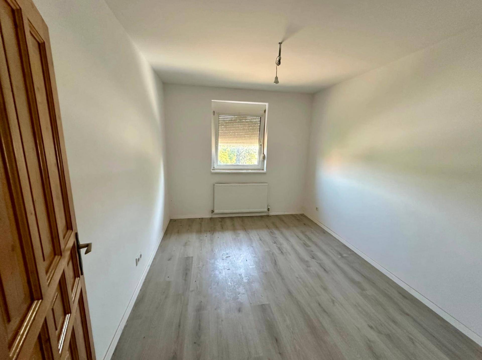 Helles, leeres Zimmer mit Laminatboden und Fenster, ideal als Schlaf- oder Kinderzimmer nach Renovierung.
