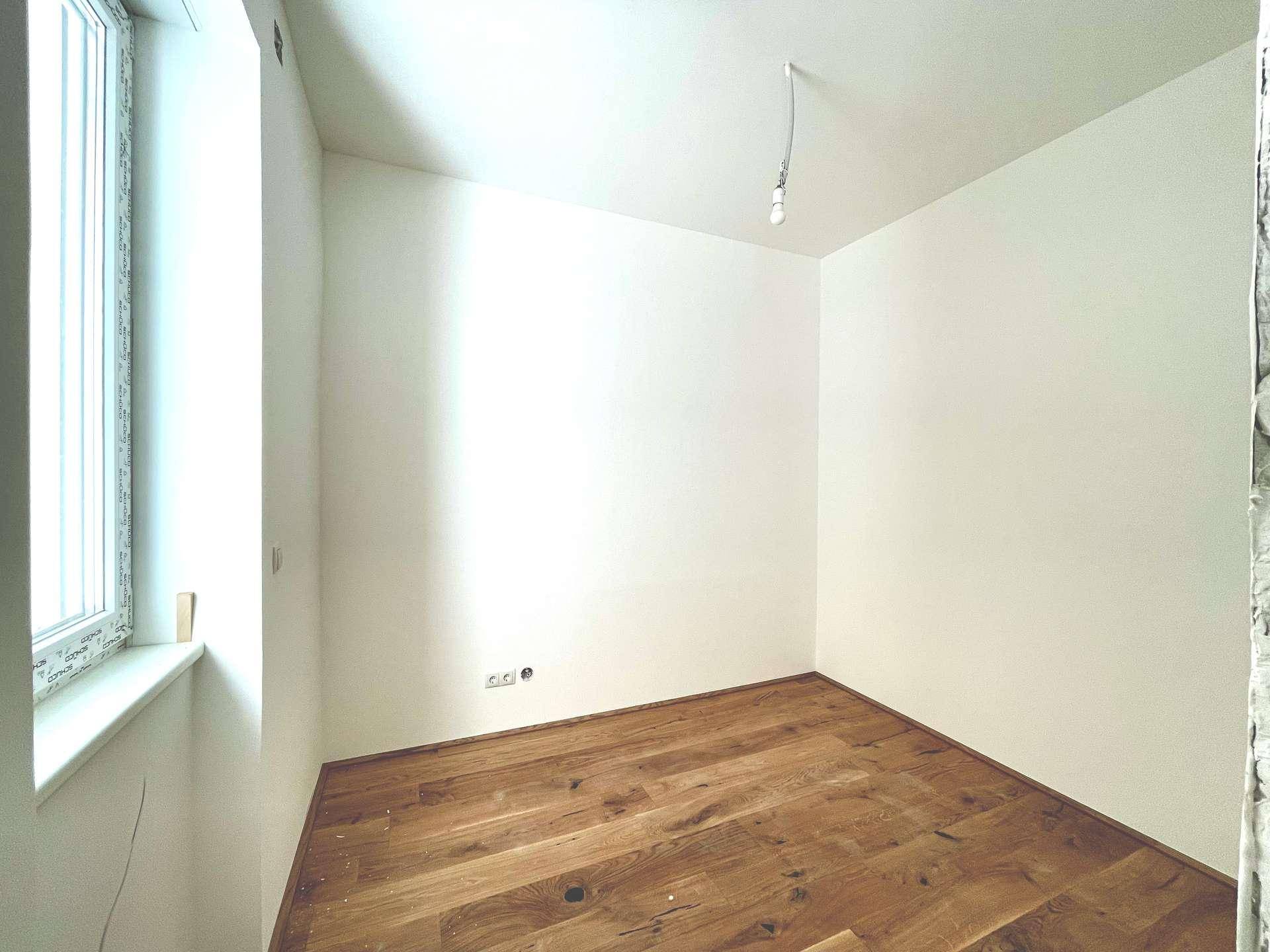 Kleiner, heller Raum mit Holzboden und einem Fenster, ideal als Kinder- oder Gästezimmer.