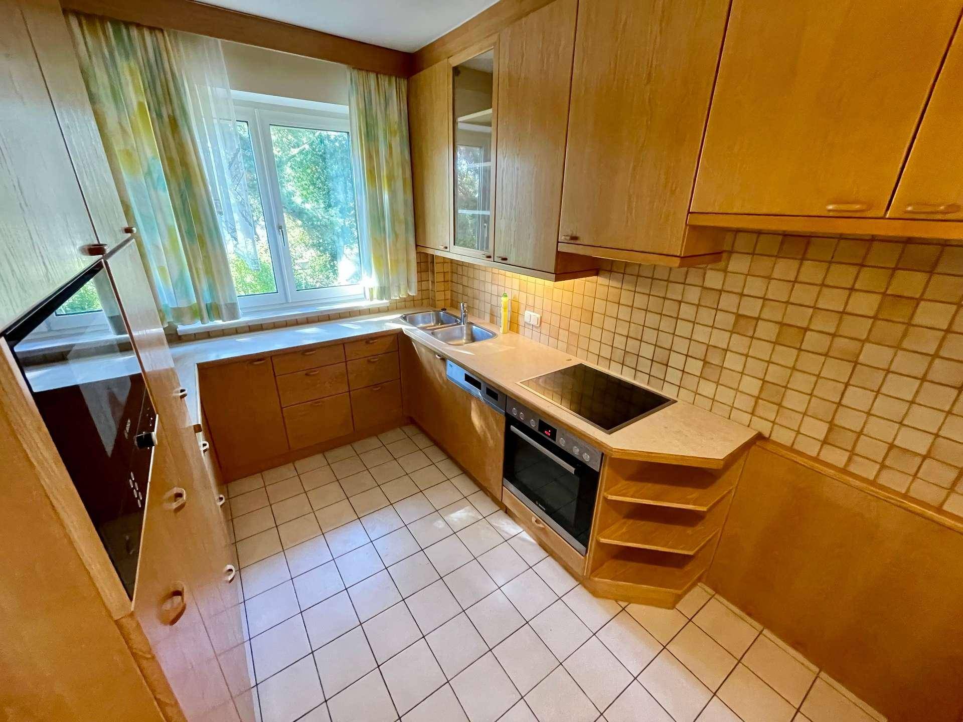 Traditionelle Holzküche mit Fliesenboden, Einbaugeräten und Fensterblick ins Grüne.