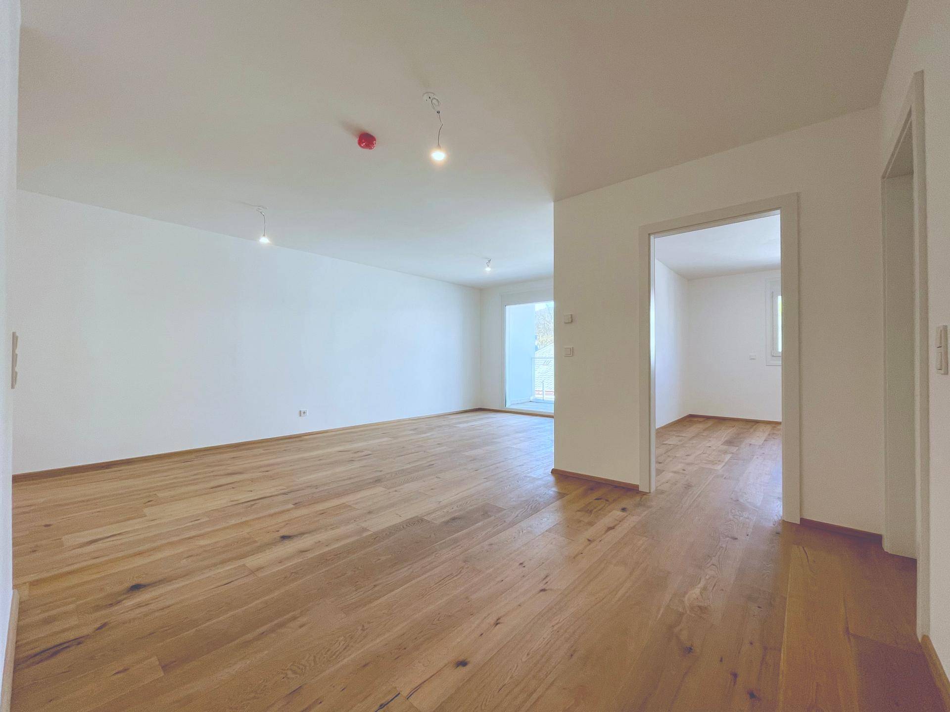 Helles Wohnzimmer mit Holzboden und Zugang zu weiteren Räumen, bietet eine offene Wohnatmosphäre.
