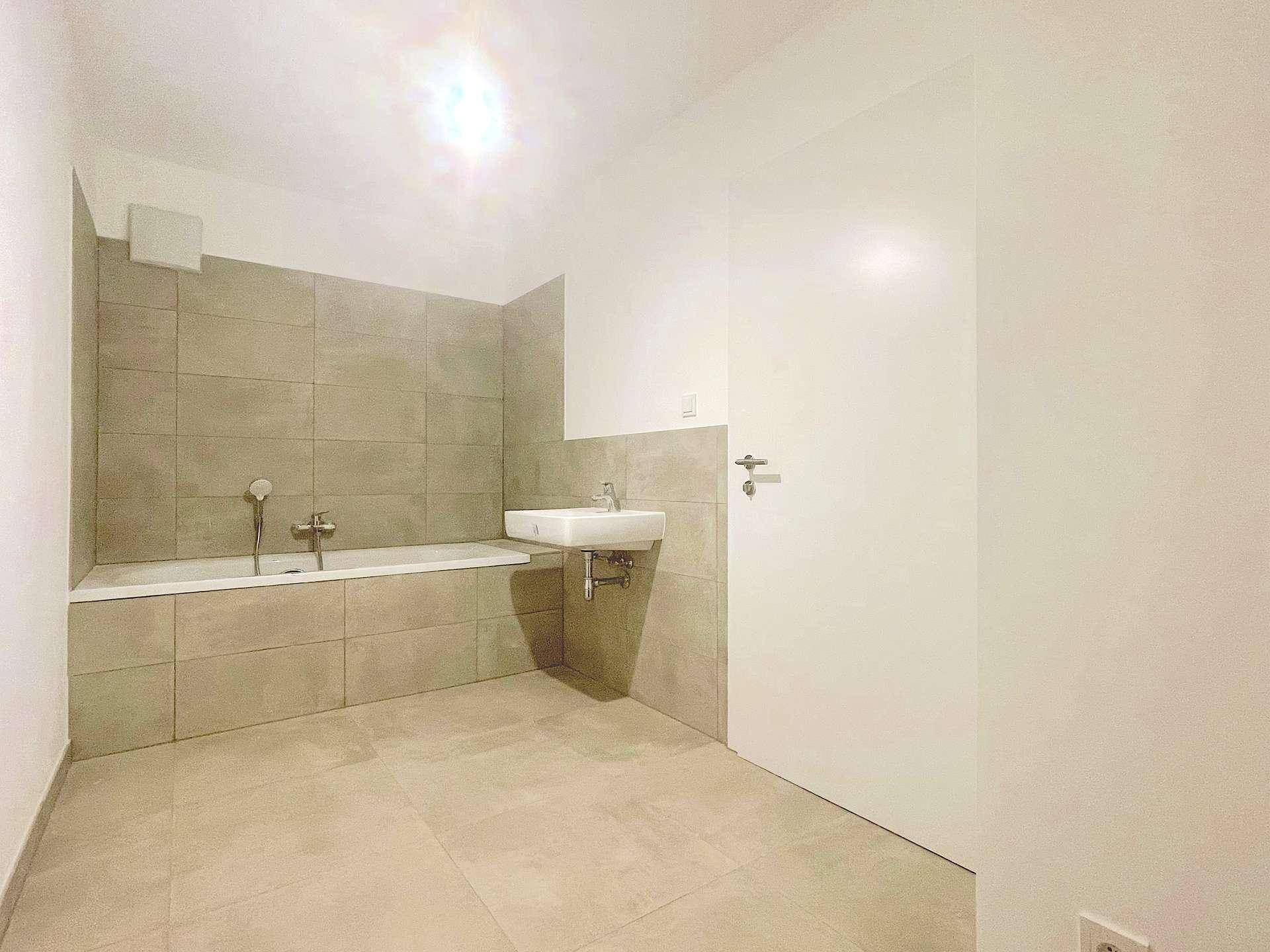 Modernes Badezimmer mit Badewanne, Waschbecken und hellen Fliesen an Wänden und Boden.
