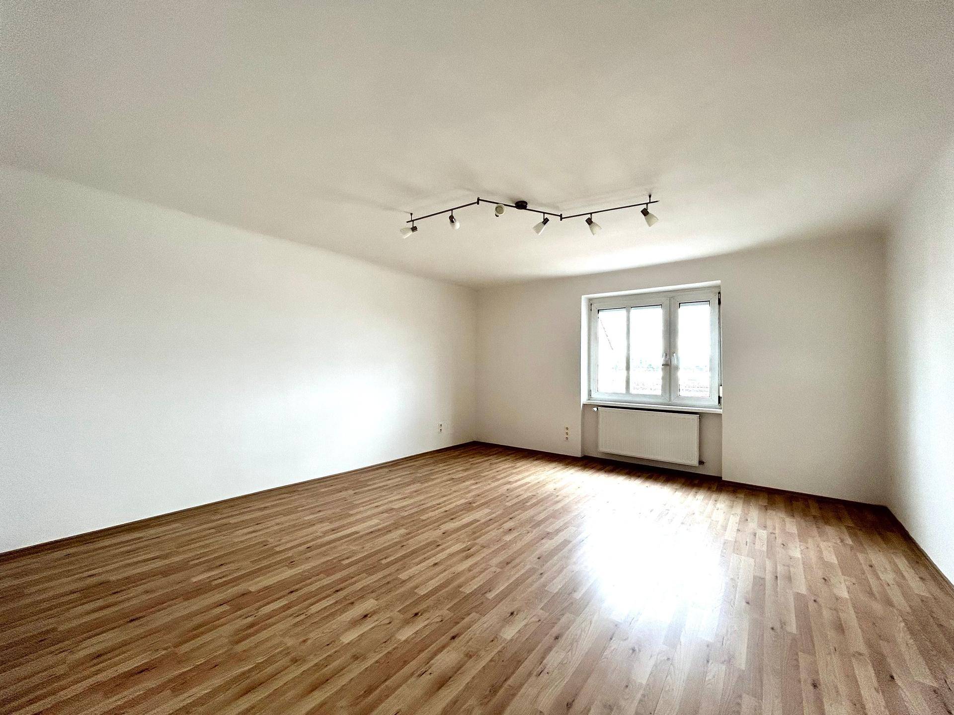 Geräumiger, heller Wohnbereich mit Holzfußboden und moderner Deckenleuchte.