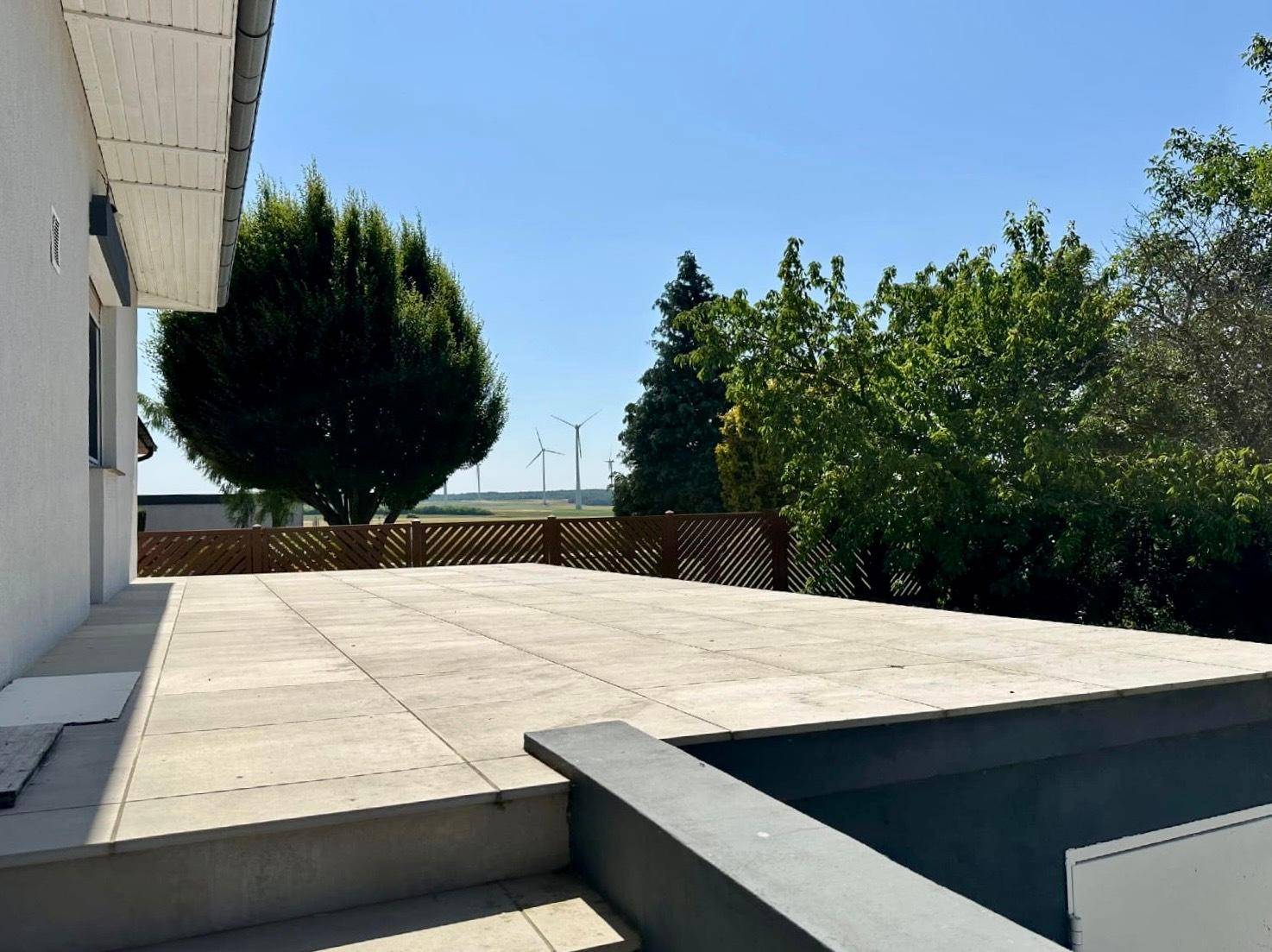 Große, gepflasterte Terrasse mit weitem Blick auf die Landschaft und Windräder am Horizont.