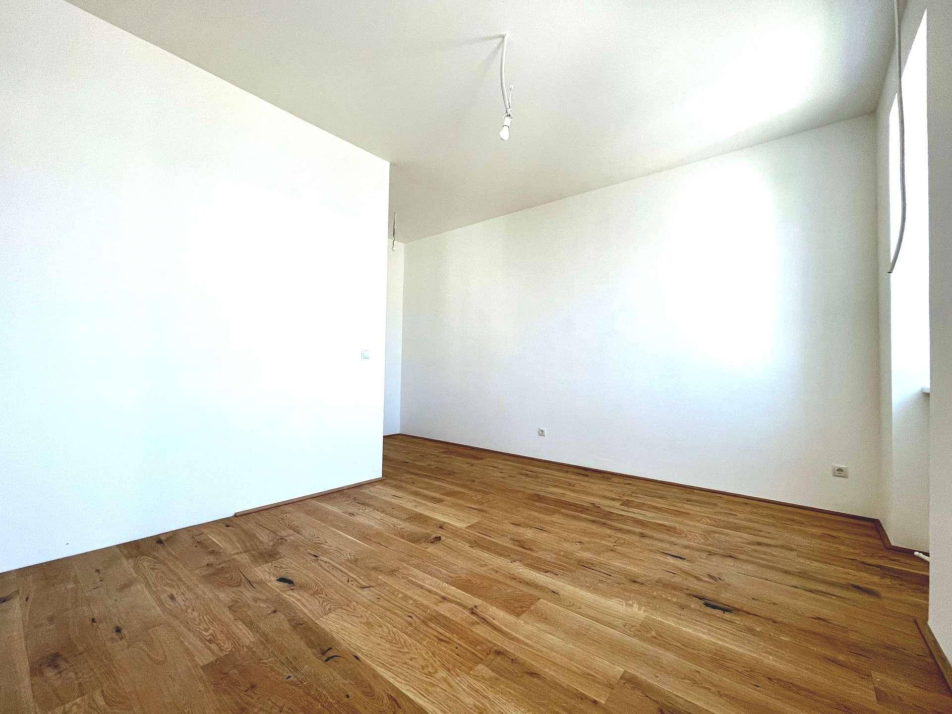 Eckbereich eines hellen Raumes mit neuem Holzboden und weißen Wänden, unmöbliert.