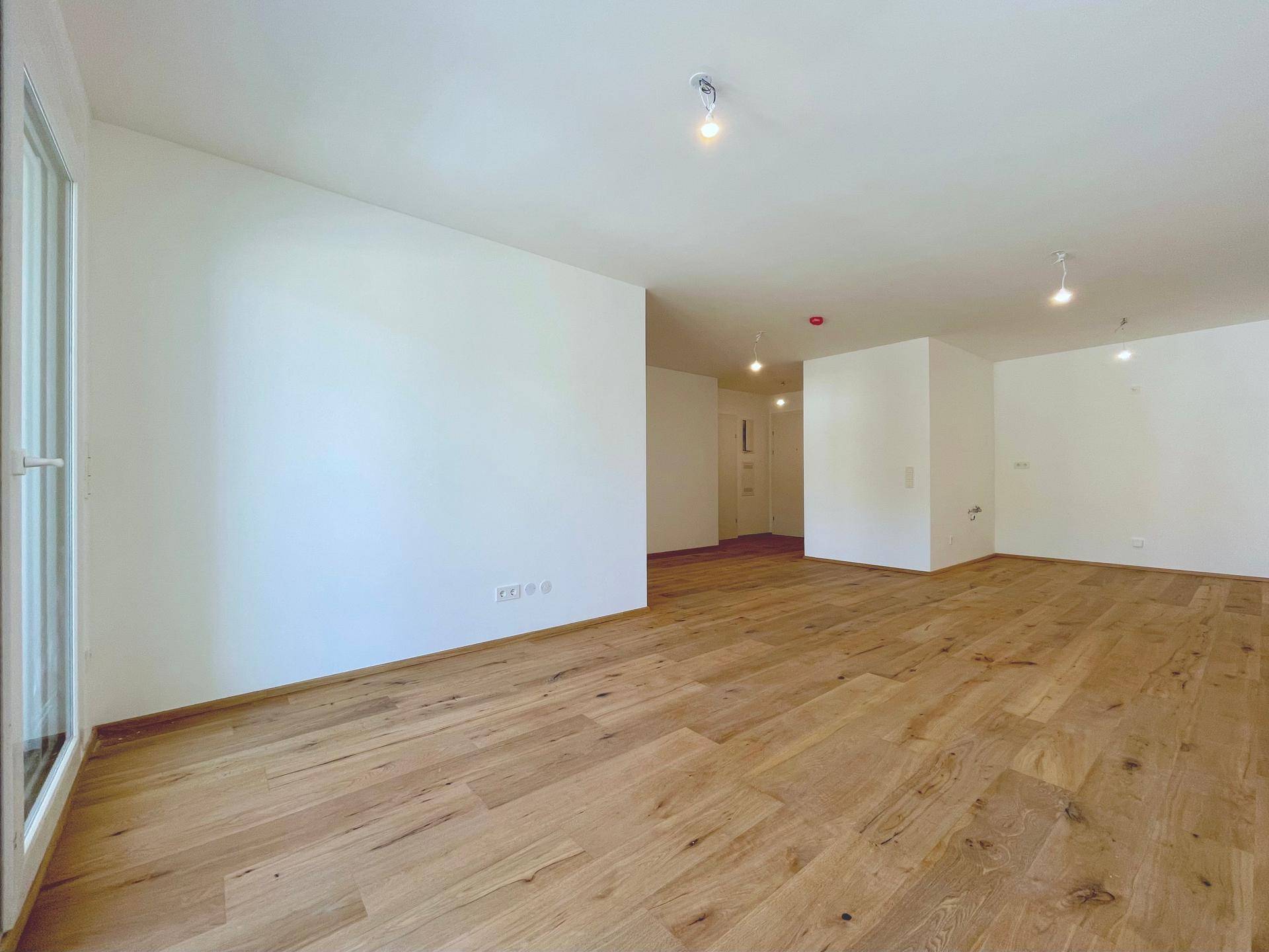 Geräumiges Wohnzimmer mit hellem Holzboden und weiß gestrichenen Wänden, ideal für individuelle Einrichtung.