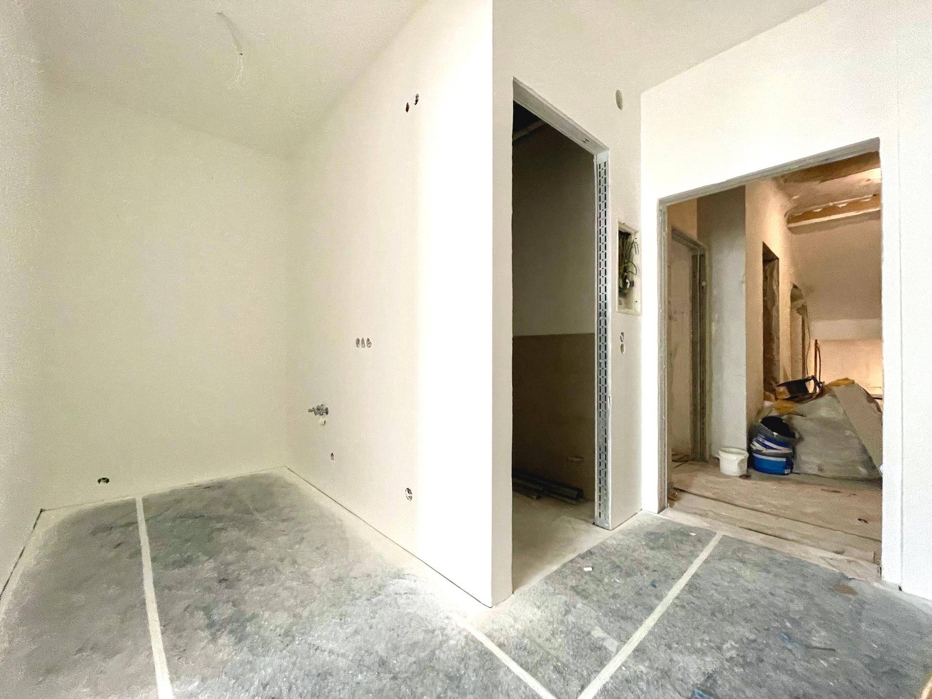 Unfertiger Innenraum mit Rohbauwänden und sichtbaren Installationen, bereit für den weiteren Ausbau.
