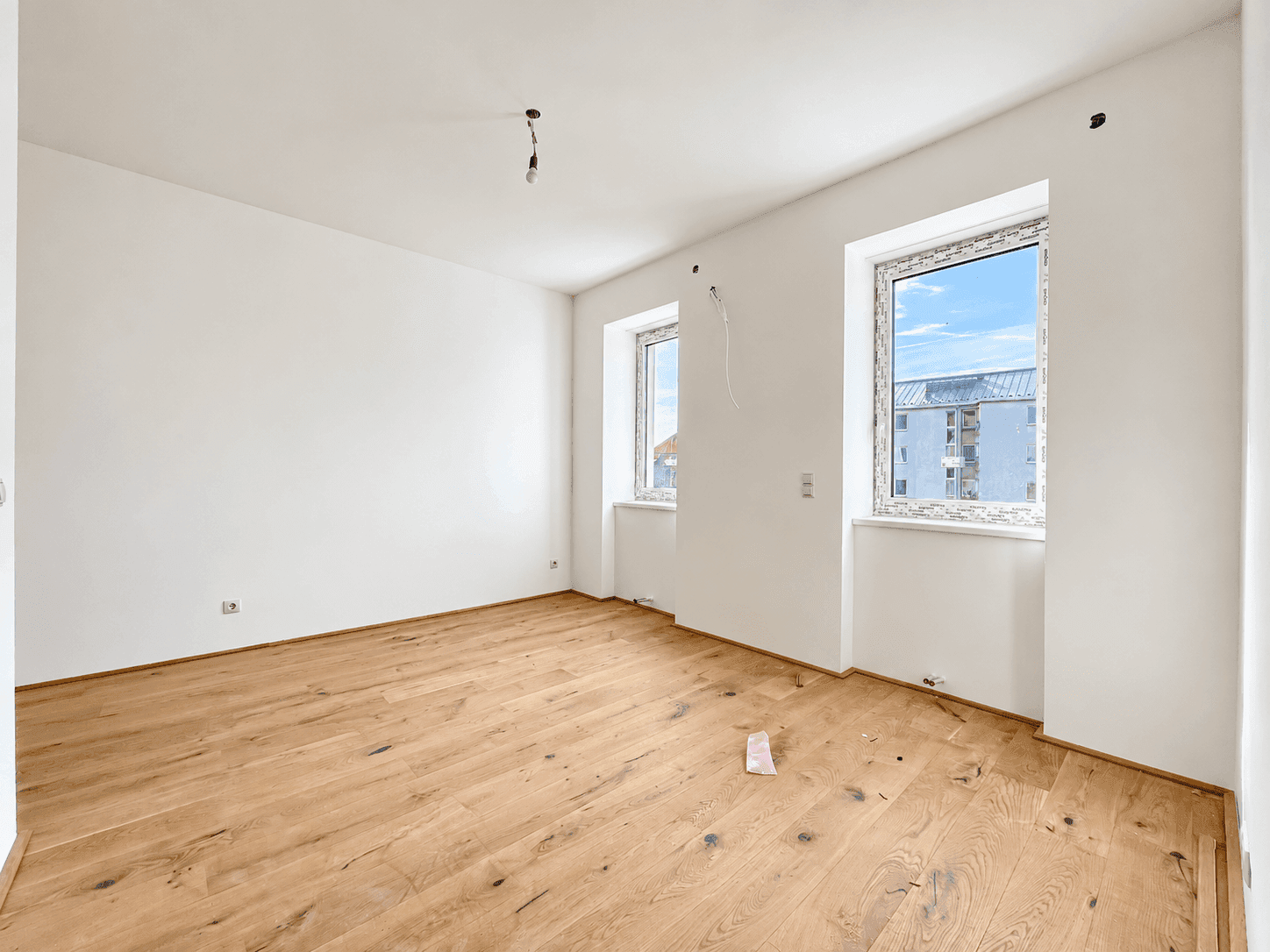 Leerer Raum mit Holzboden und Fenstern, die einen Blick auf die Umgebung bieten.
