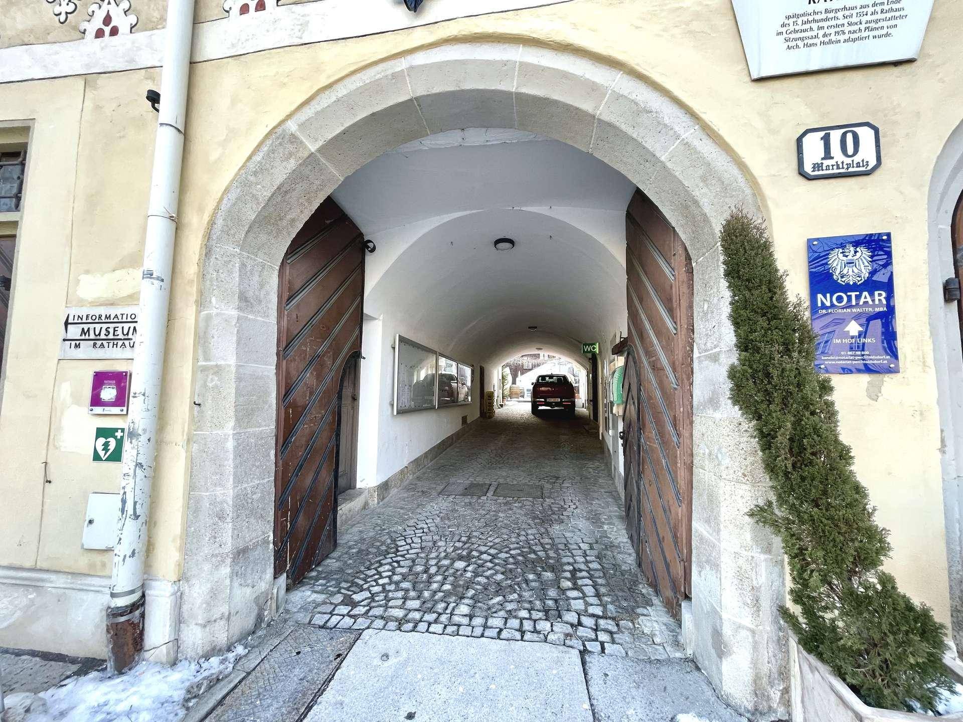 Historischer Torbogen mit Holztoren, der zu einem gepflasterten Durchgang führt.
