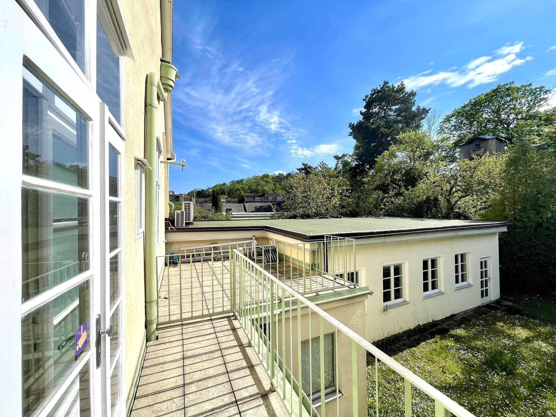 Heller Balkon mit Metallgeländer und Blick auf grüne Bäume und umliegende Gebäude.