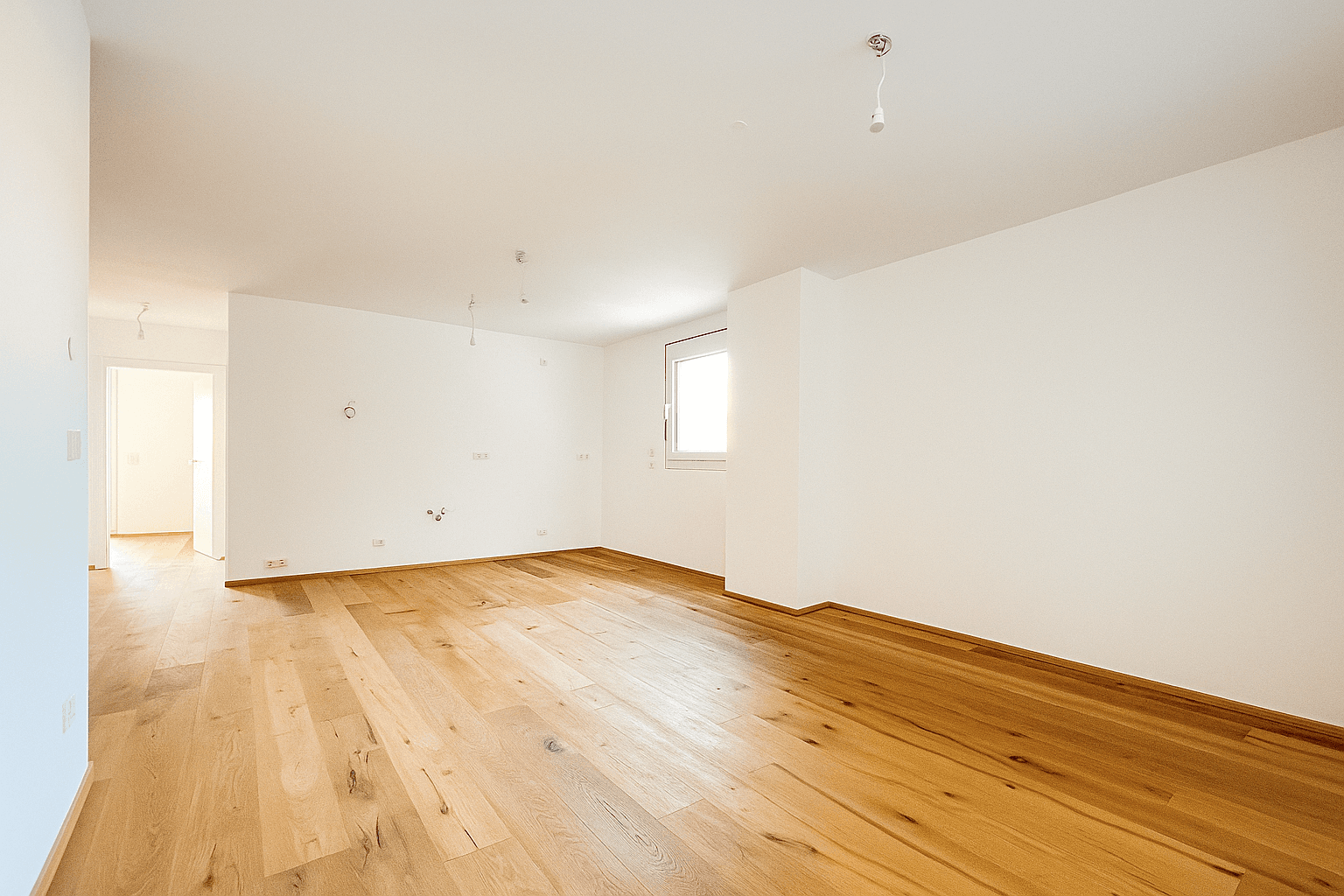 Heller, leerer Wohnraum mit Holzboden und großen Fenstern, die viel Tageslicht hereinlassen.