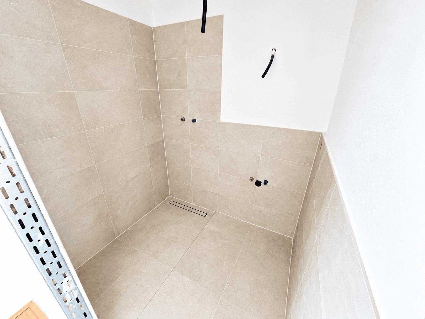 Unfertiges Badezimmer mit beigefarbenen Fliesen, vorbereitet für Sanitärinstallationen.