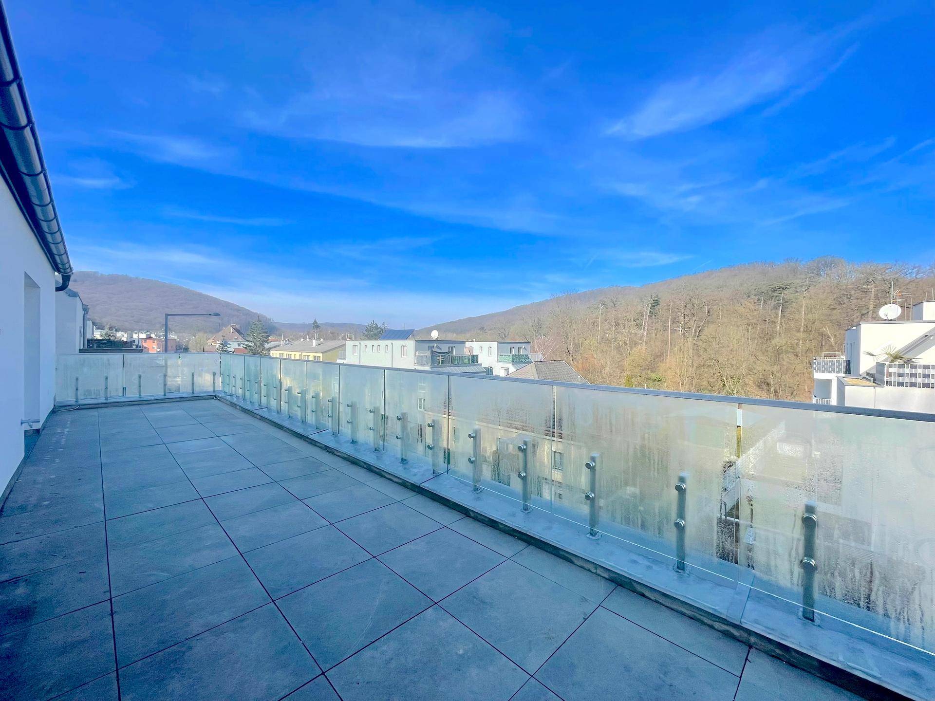 Weitläufige Dachterrasse mit Fliesenboden und Glasgeländer, bietet einen Panoramablick auf die Hügel.