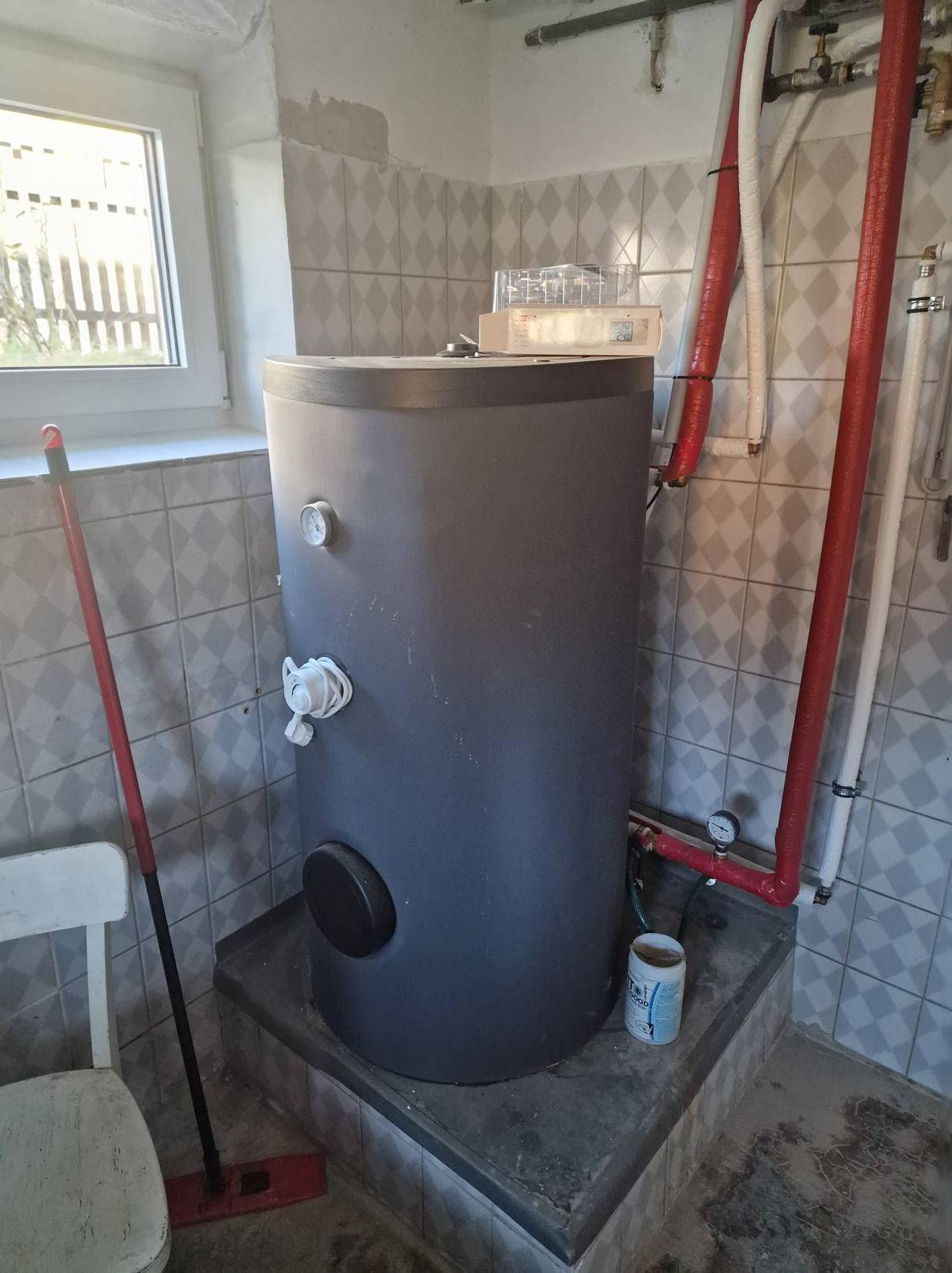 Großer Warmwasserspeicher in einem gefliesten Raum mit Fenster.