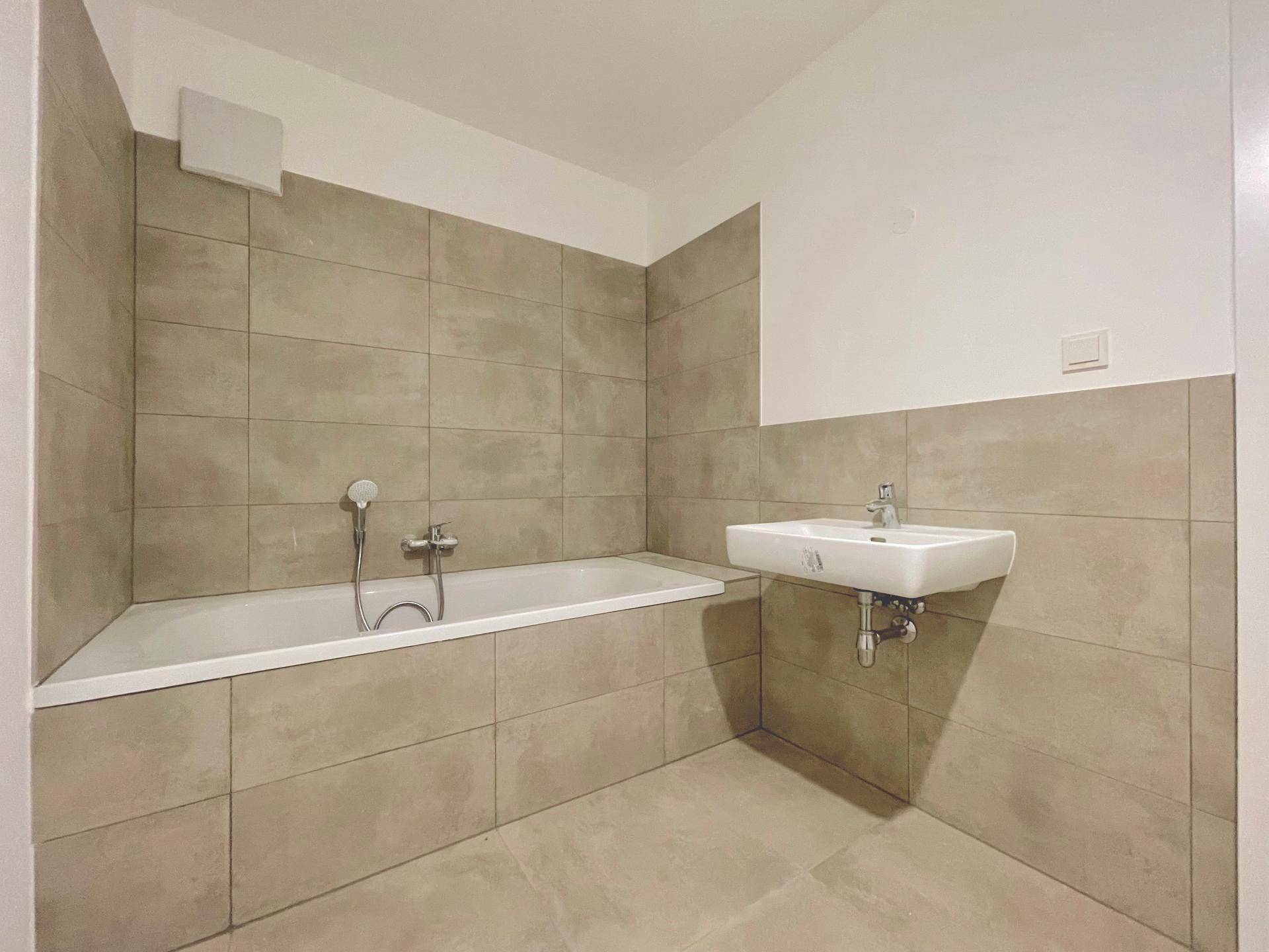 Modernes Badezimmer mit Badewanne, Waschbecken und beigefarbenen Fliesen, in neuwertigem Zustand.