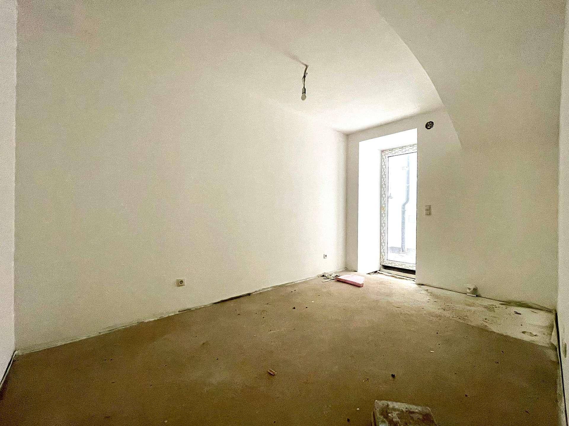 Kleinerer Raum im Rohbau mit Betonboden und Fenstertür, ideal als Schlaf- oder Arbeitszimmer.