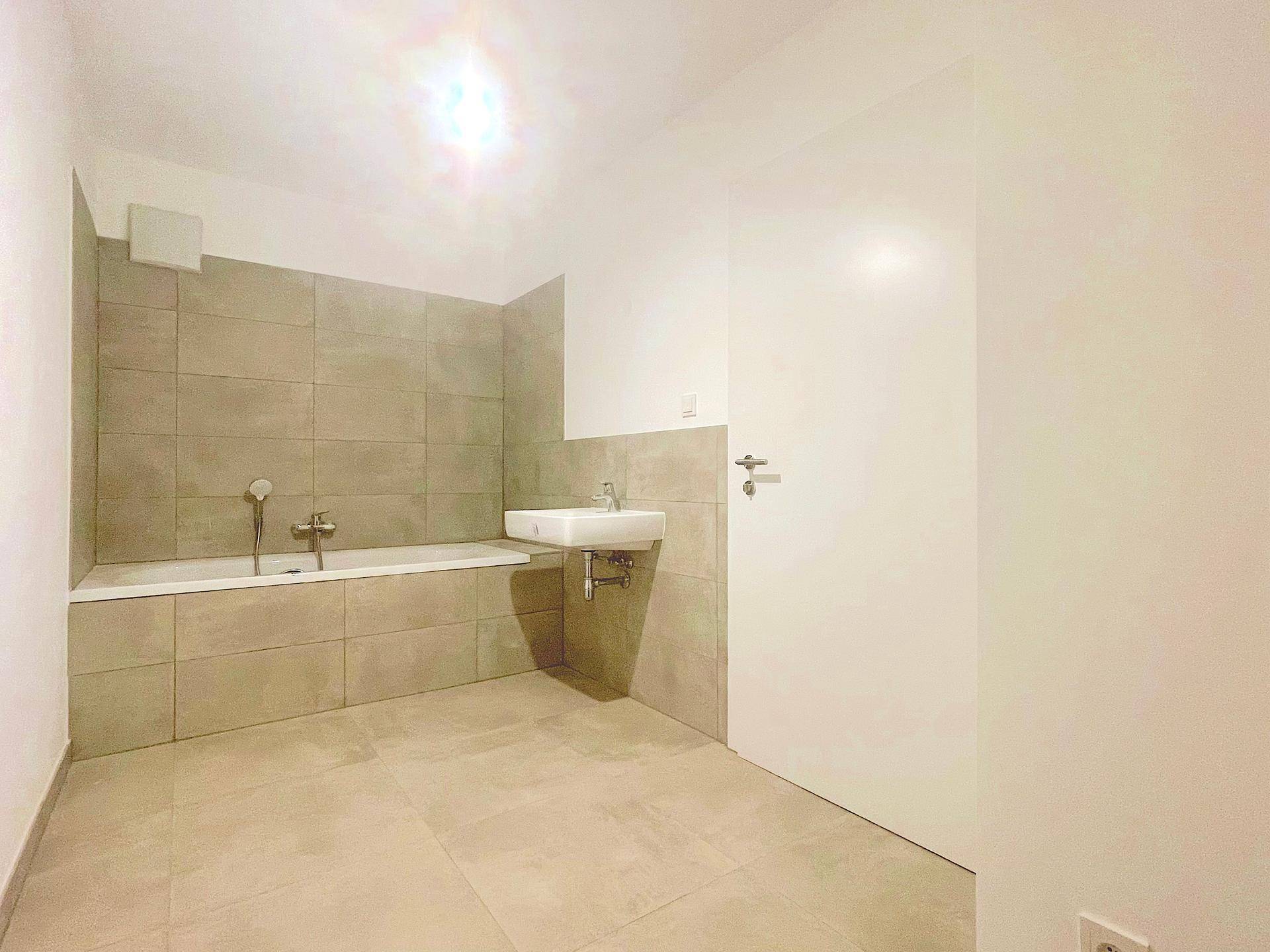 Modernes Badezimmer mit Badewanne und beigefarbenen Fliesen an Wänden und Boden.