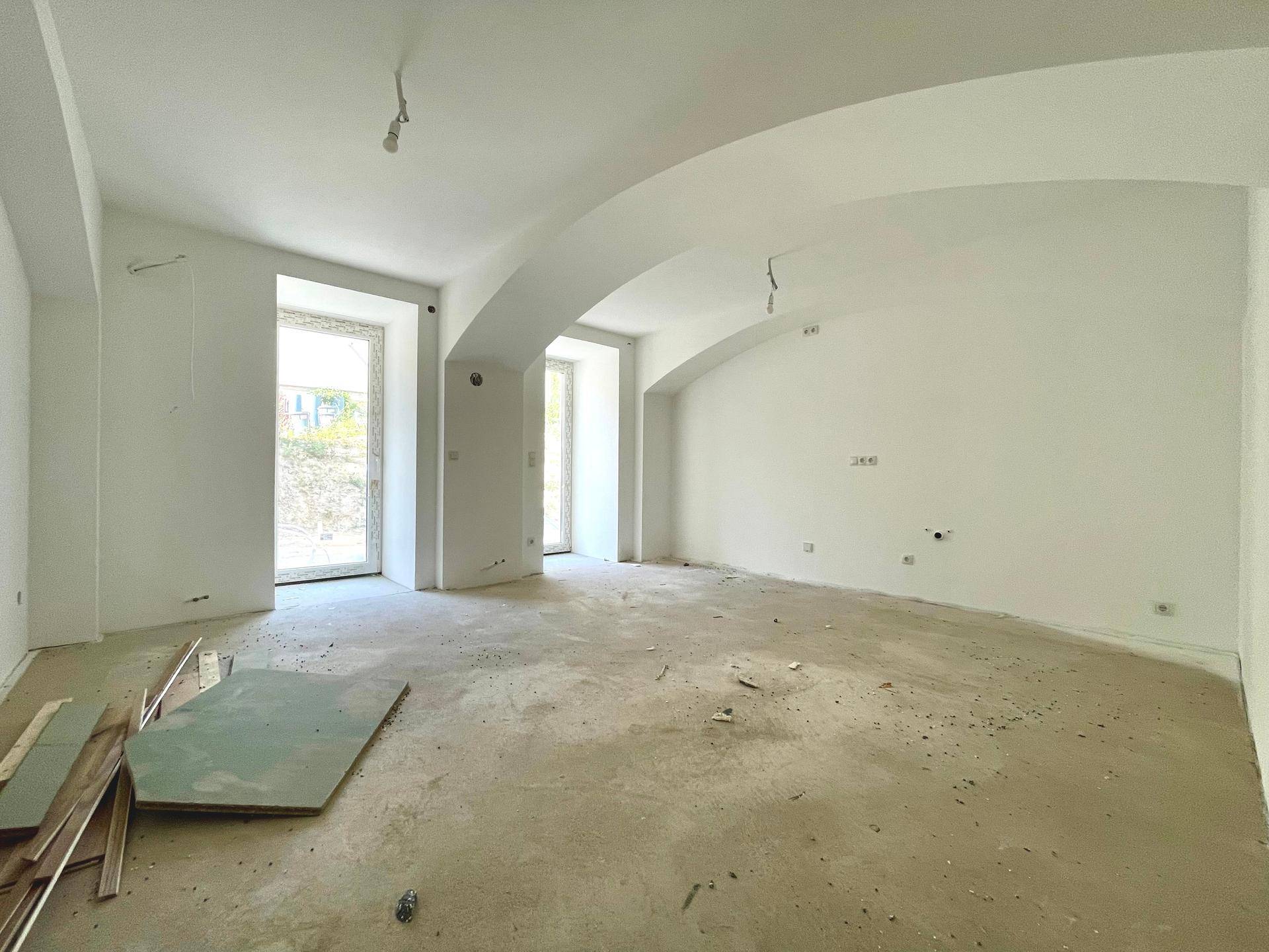 Weiter Raum im Rohzustand mit Gewölbedecken und Fenstertüren, bereit für den Ausbau.