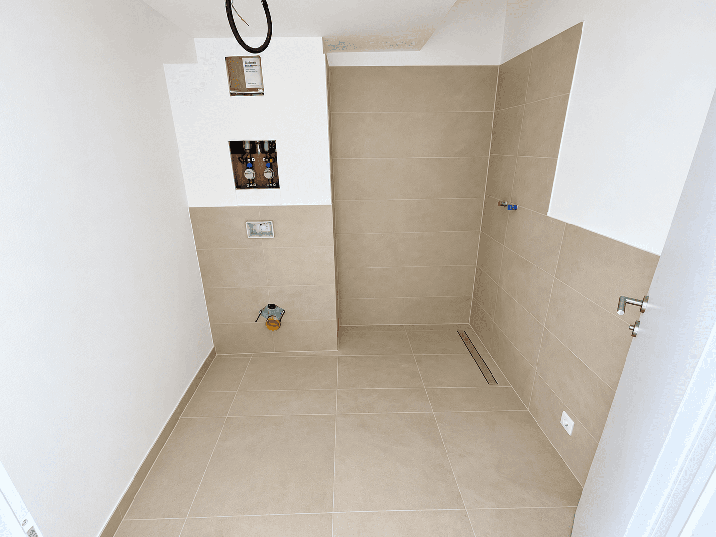 Modernes Badezimmer im Rohbau mit beigefarbenen Fliesen und vorbereiteter Duschfläche.