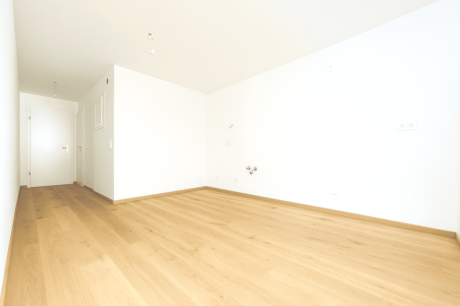 Heller, leerer Wohnraum mit Holzboden und großen Fenstern, die viel Tageslicht hereinlassen.