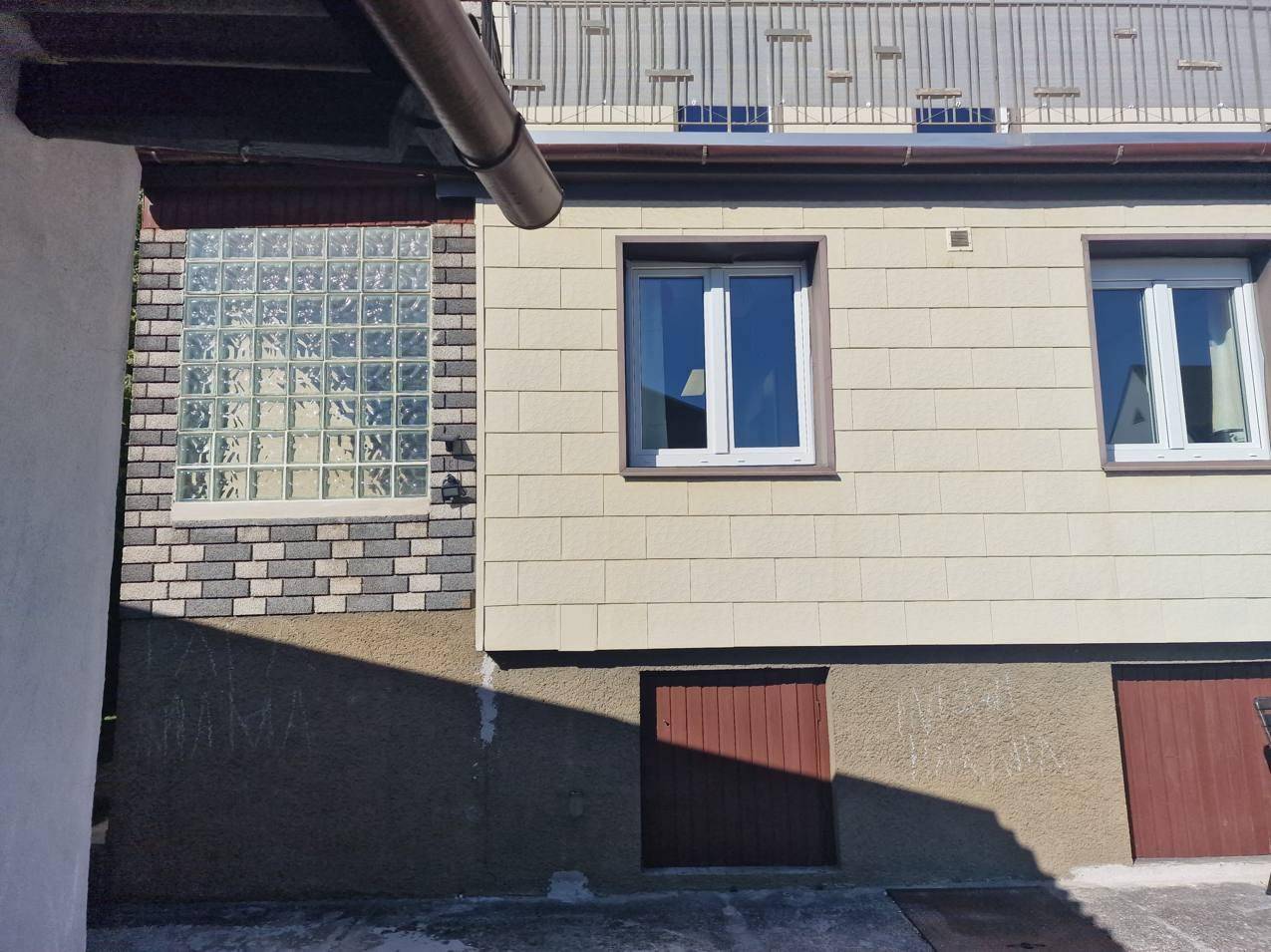 Detail der Hausfassade mit Glasbausteinen und einer kleinen Holztür im unteren Bereich.