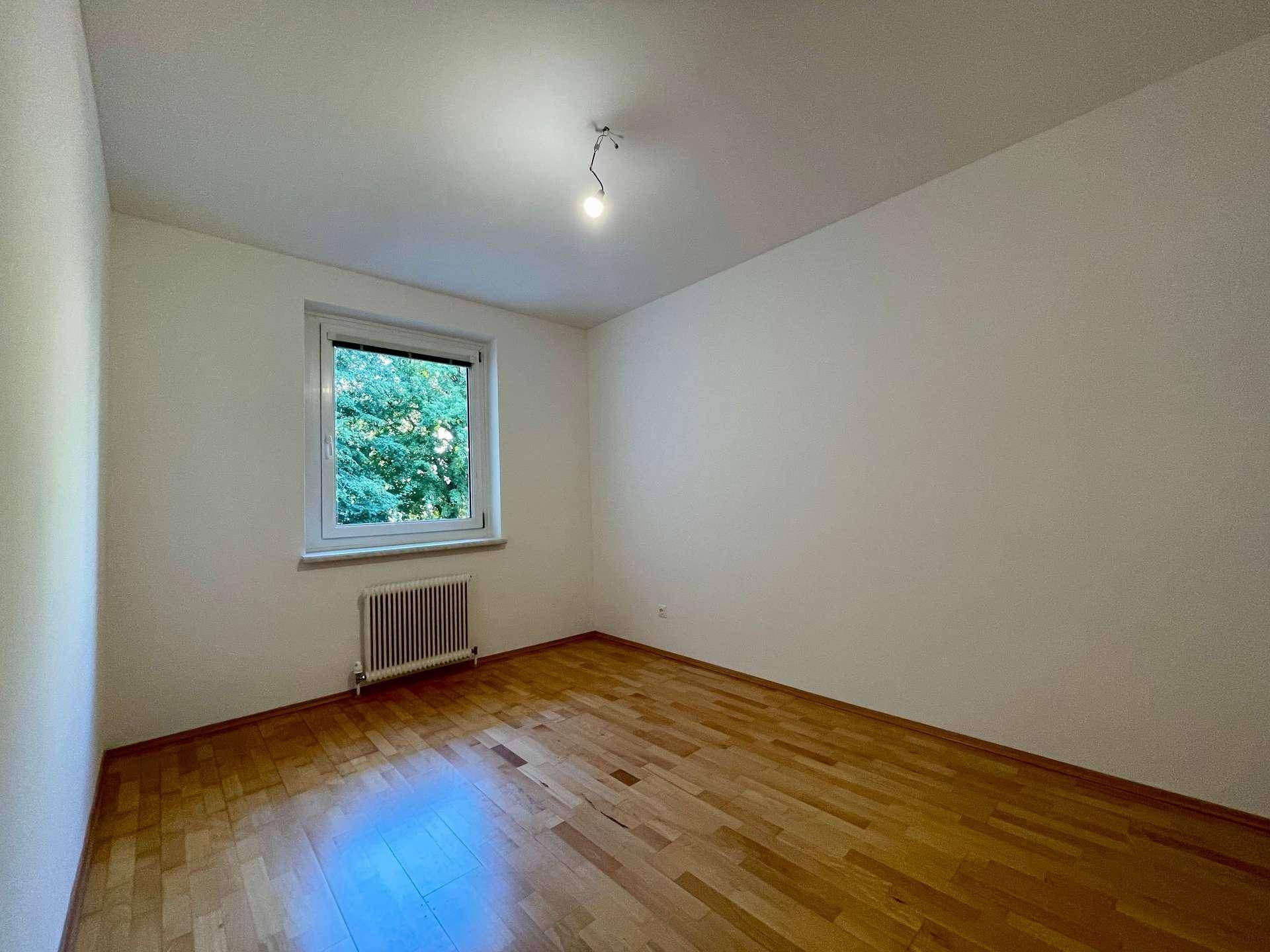 Gemütliches Zimmer mit Parkettboden und einem Fenster, das einen ruhigen Blick ins Grüne ermöglicht.
