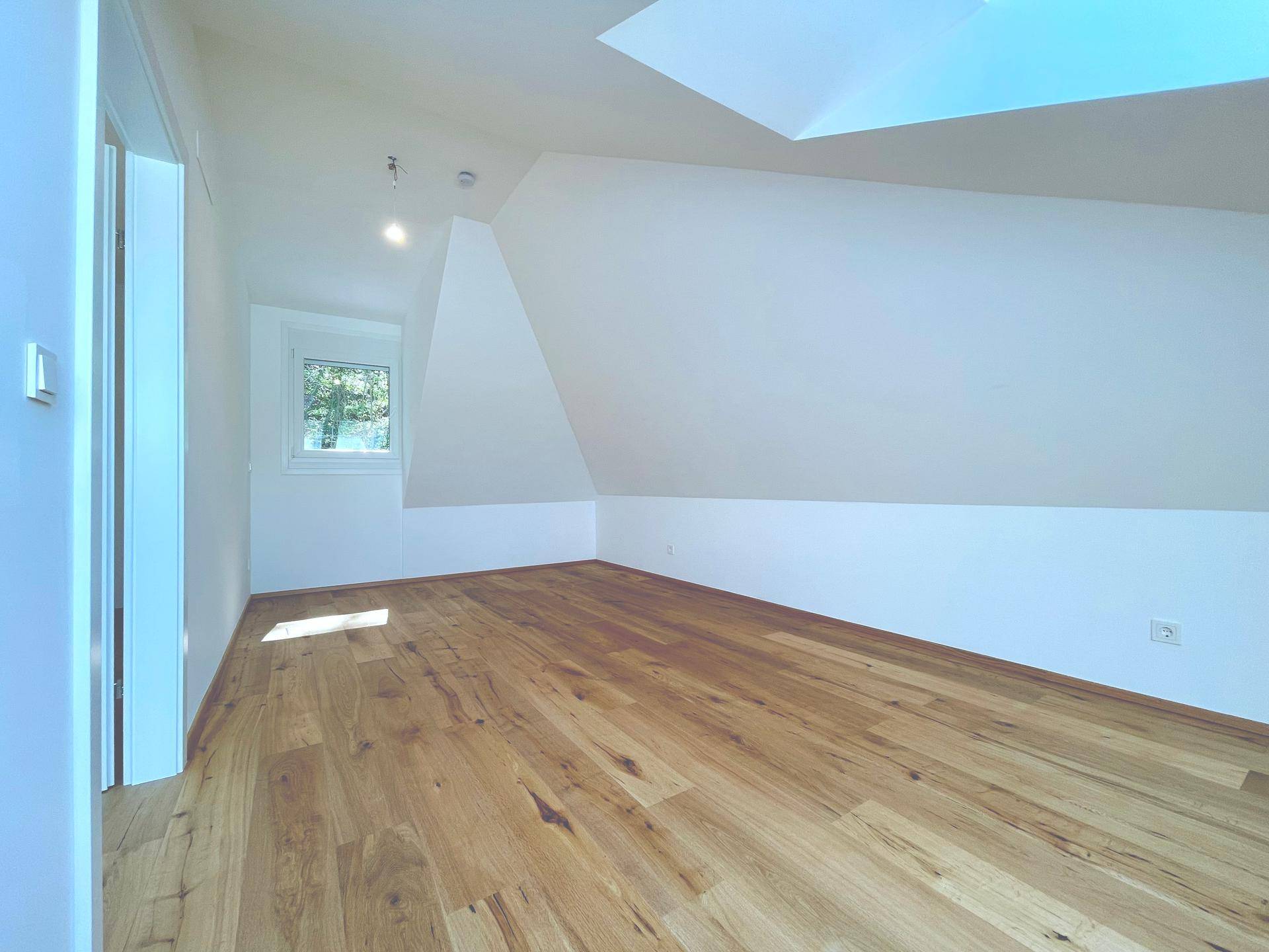 Helles Schlafzimmer im Dachgeschoss mit Holzboden und Fenster, bietet eine ruhige und angenehme Atmosphäre.
