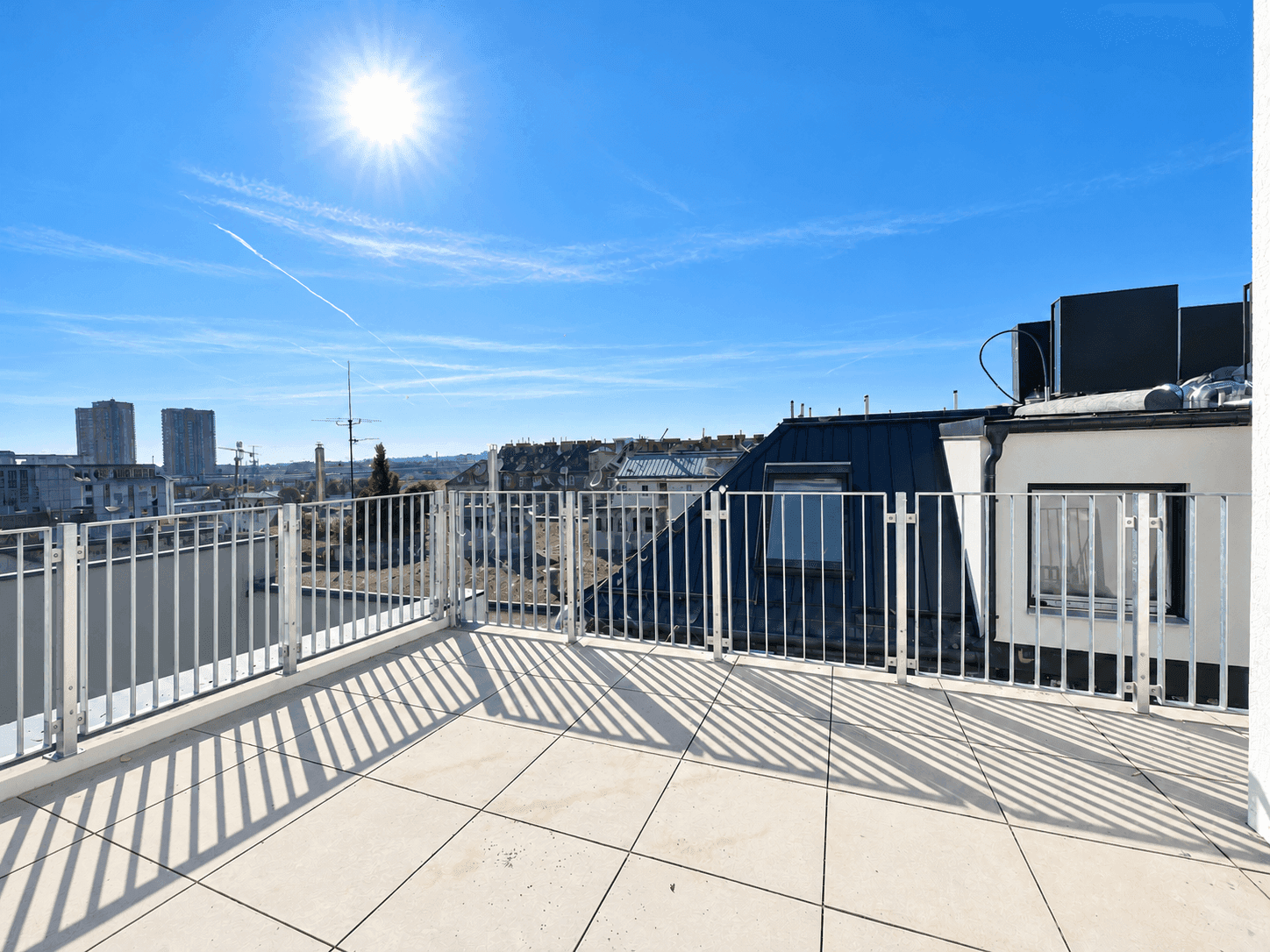 Heller Balkon mit Fliesenboden und Panoramablick auf die Stadt unter blauem Himmel.