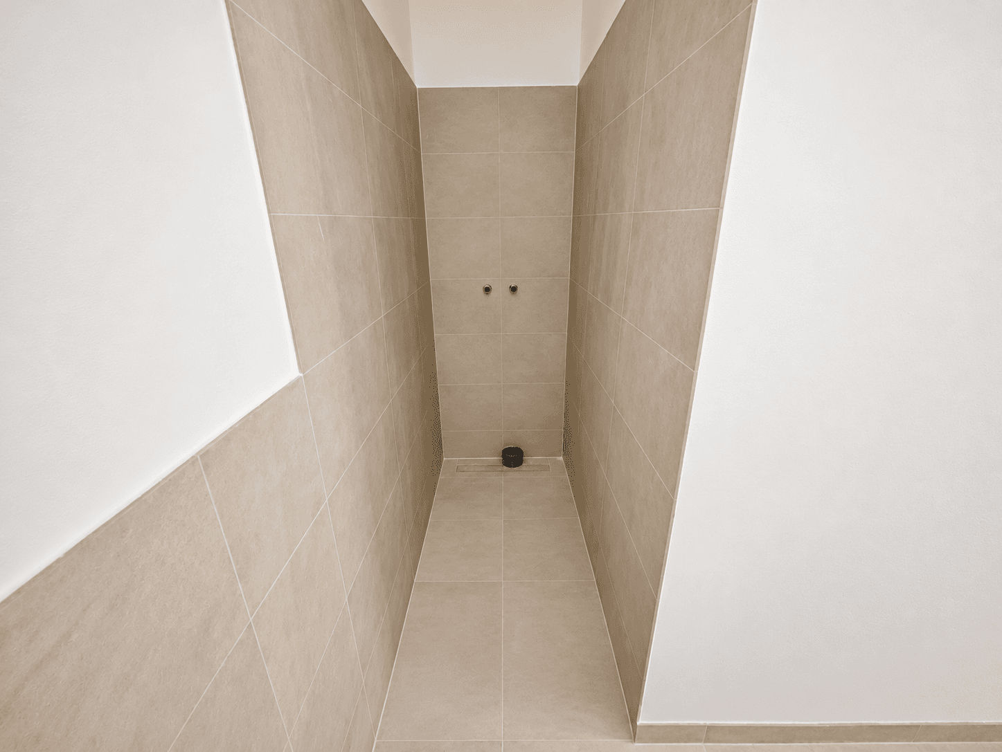 Unfertiger Duschbereich mit beigefarbenen Wand- und Bodenfliesen, bereit für die Installation der Armaturen.