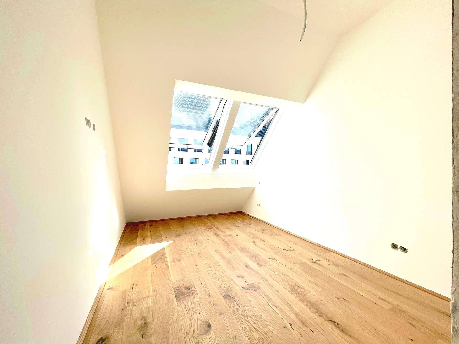 Lichtdurchflutetes Zimmer mit Holzboden und schrägem Dach, ideal für ein gemütliches Schlafzimmer.