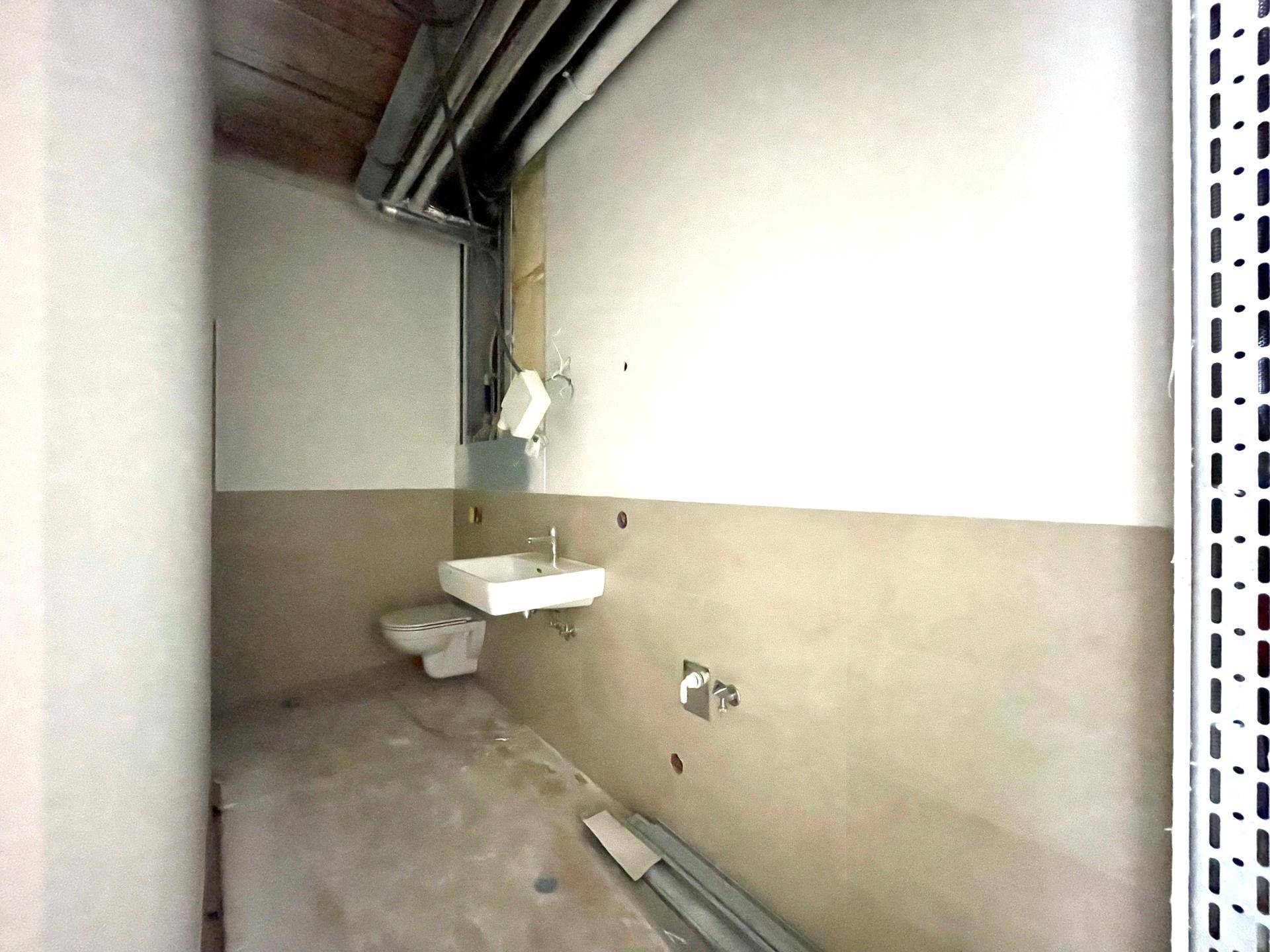 Unfertiges Gäste-WC mit wandhängender Toilette und kleinem Waschbecken, noch im Rohbauzustand.