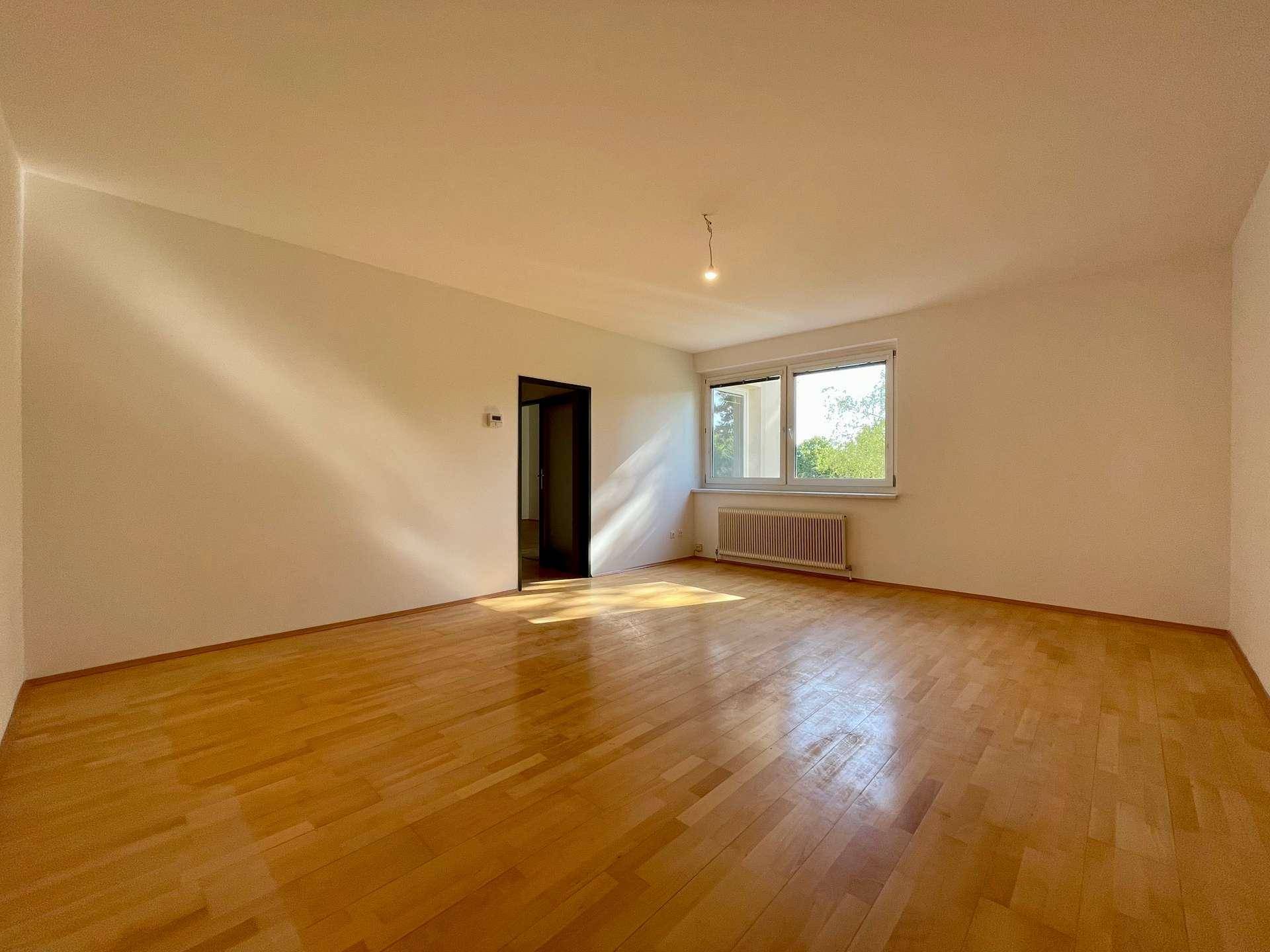 Geräumiges Zimmer mit hellem Parkettboden und großen Fenstern, die den Raum sonnig erscheinen lassen.