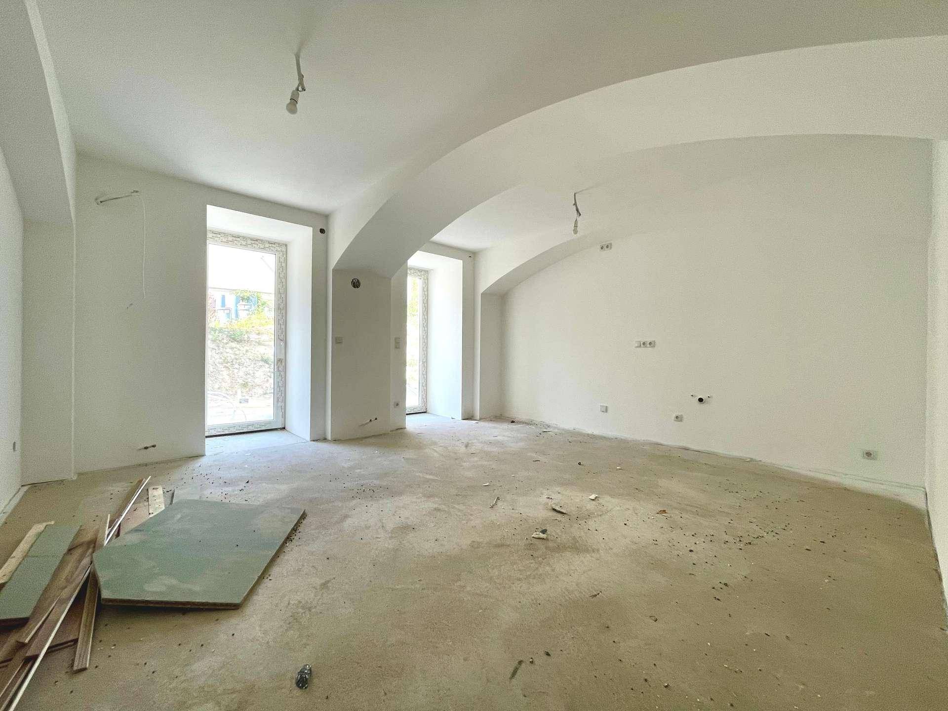 Geräumiger Wohnbereich im Rohbau mit gewölbten Decken und hohen Fenstertüren, wartet auf den Innenausbau.