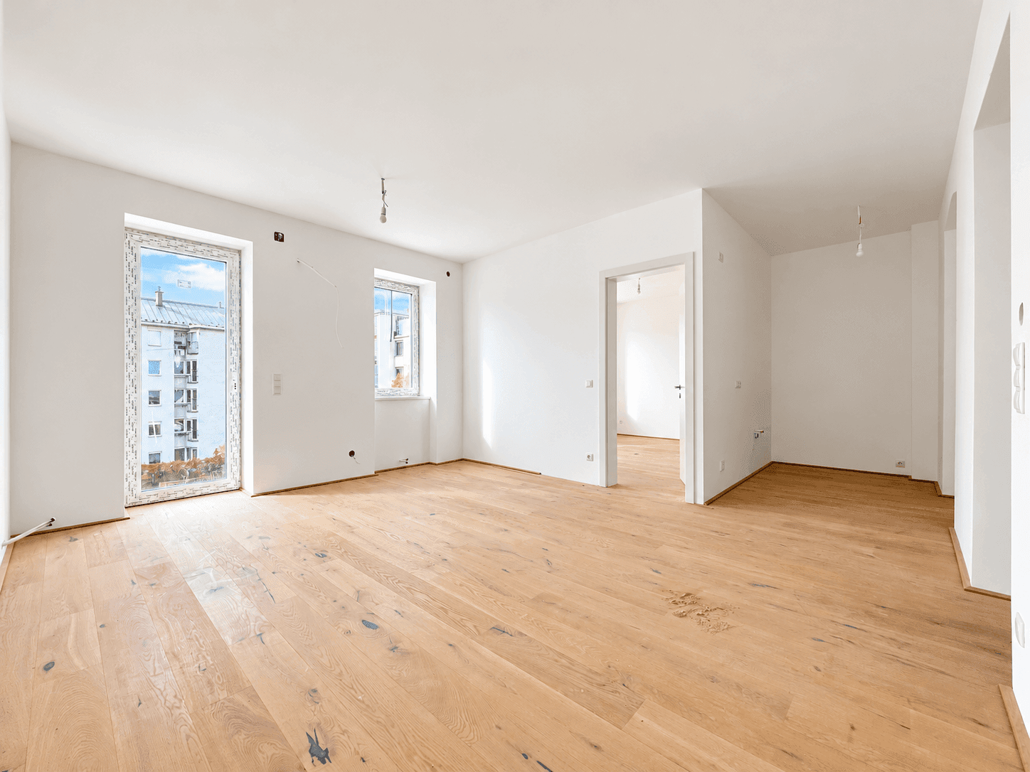 Geräumiges, unmöbliertes Zimmer mit hellem Parkettboden und Zugang zu weiteren Räumen.