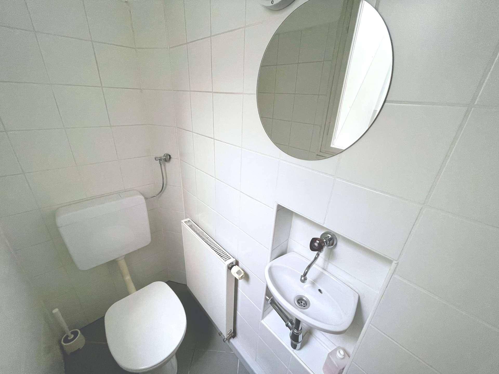 Kompakte Gästetoilette mit weißen Fliesen, kleinem Waschbecken und Heizkörper.