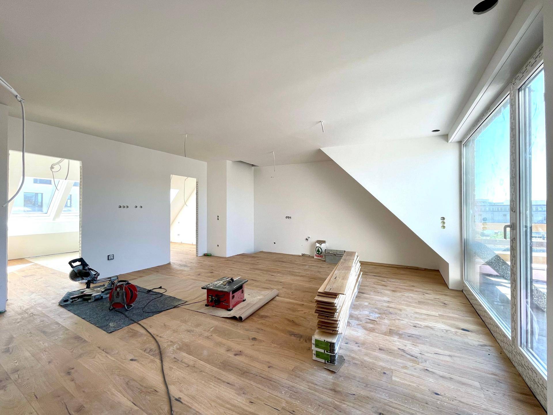Großer Wohnbereich im Dachgeschoss mit neu verlegtem Holzparkett und großen Fenstern, noch im Ausbau.