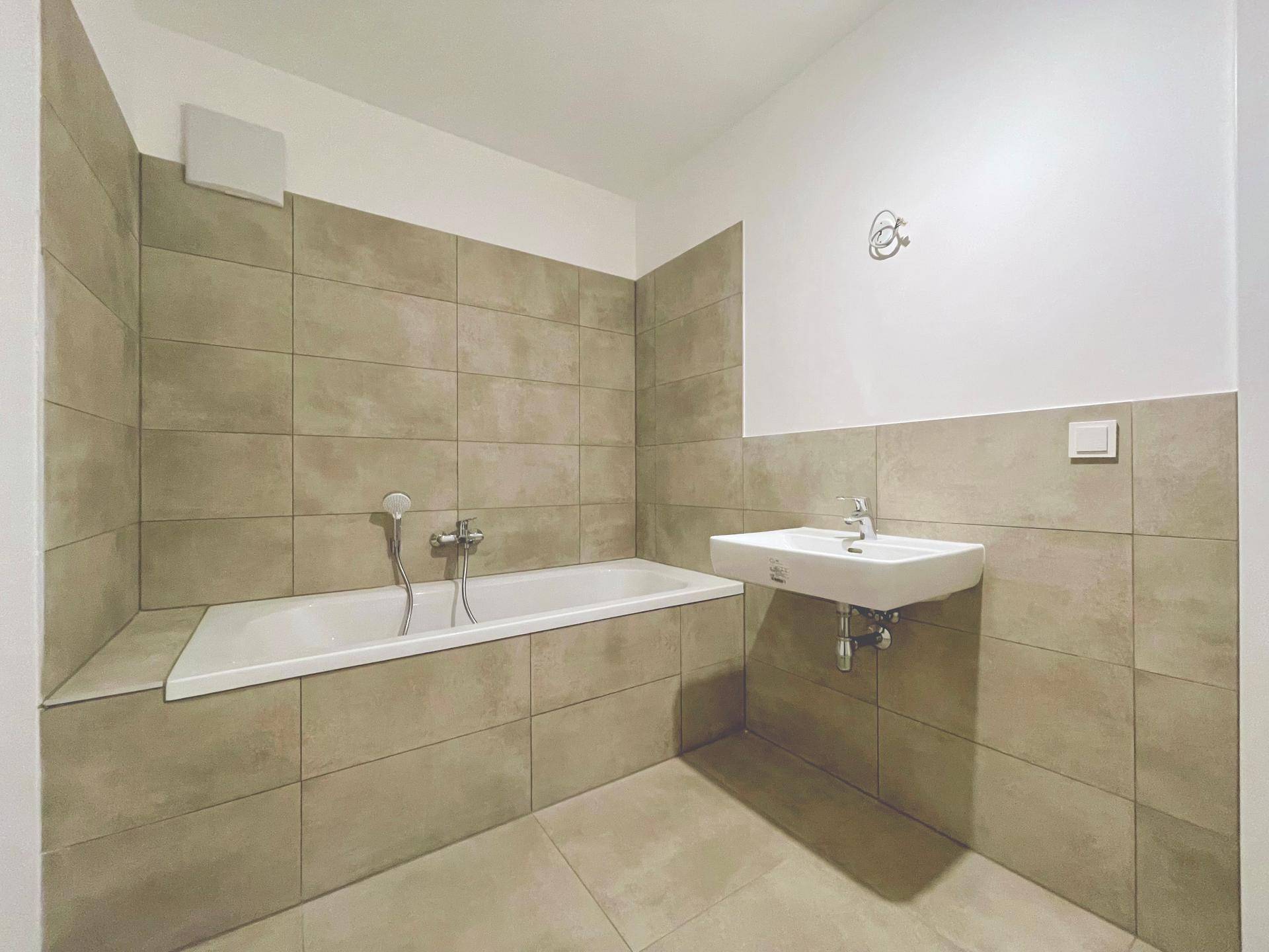 Modernes Badezimmer mit Badewanne, Waschbecken und beigefarbenen Fliesen, in neuwertigem Zustand.