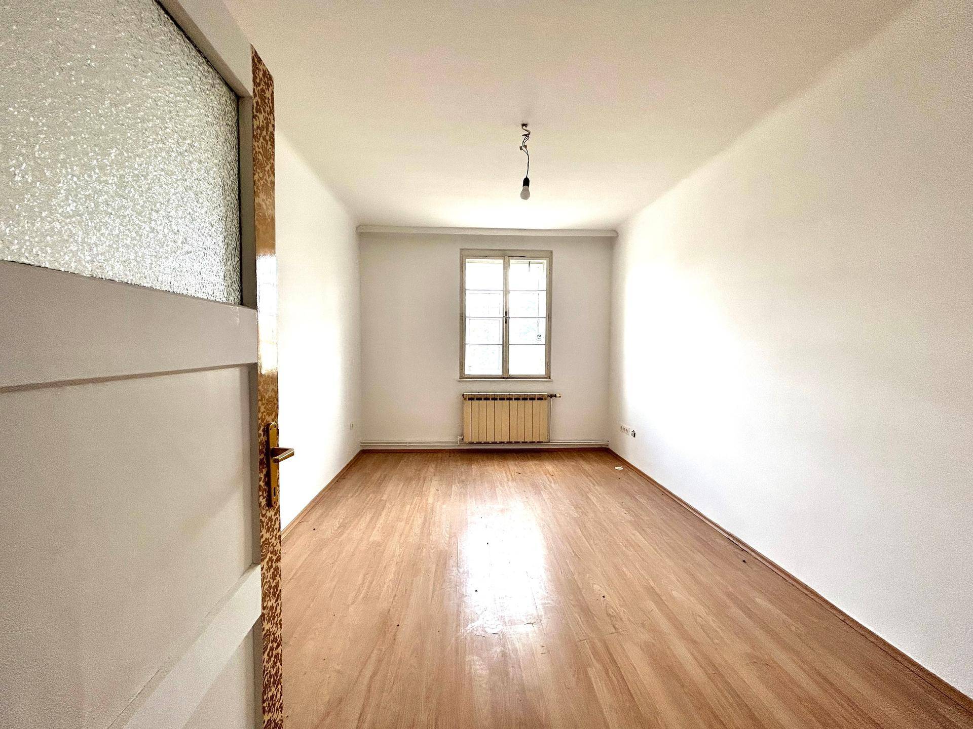 Leerer Raum mit Laminatboden und weiß gestrichenen Wänden, gesehen durch eine offene Tür.
