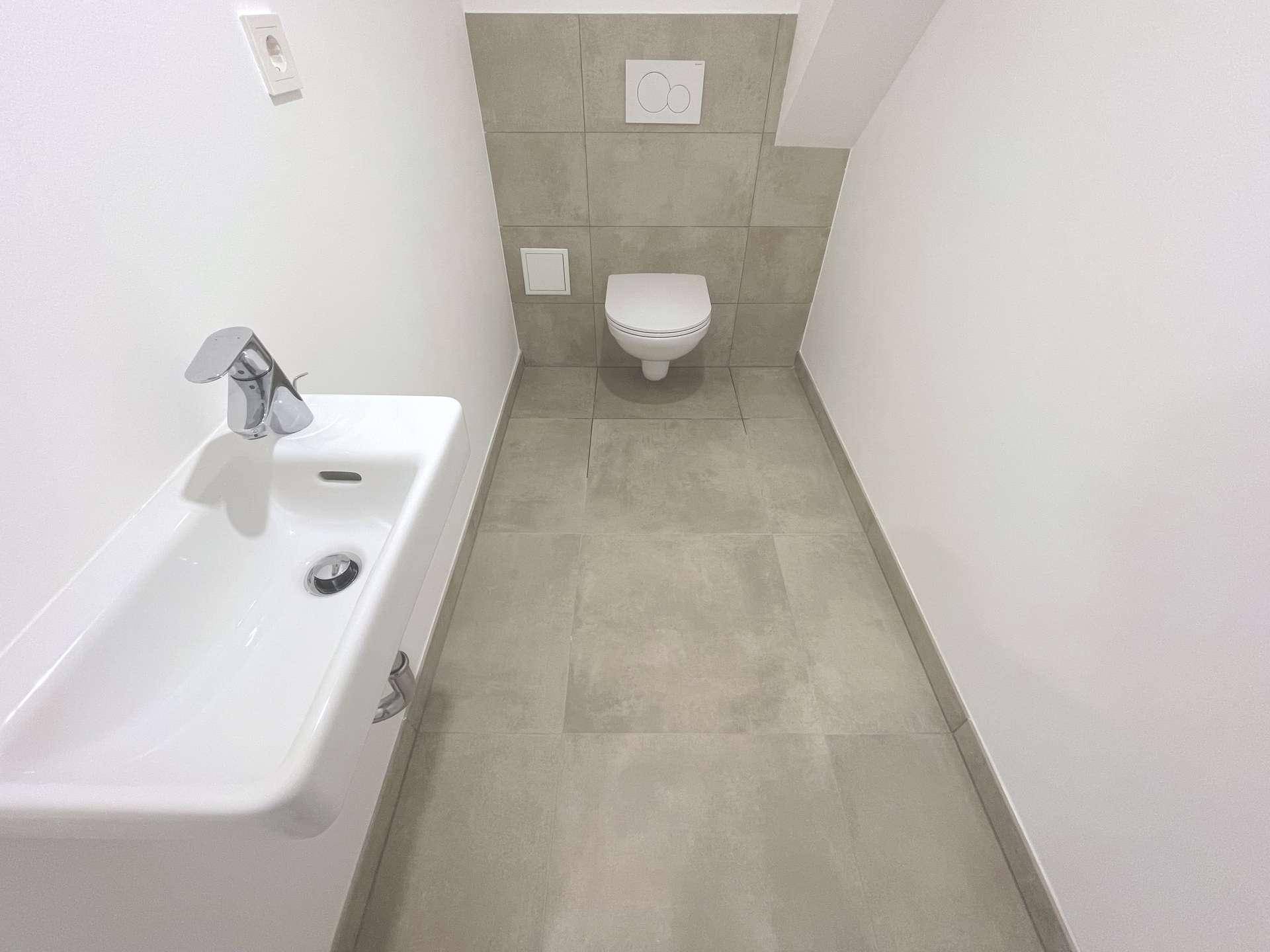 Kompaktes WC mit wandhängender Toilette und modernem Waschbecken, in neutralen Grautönen gehalten.